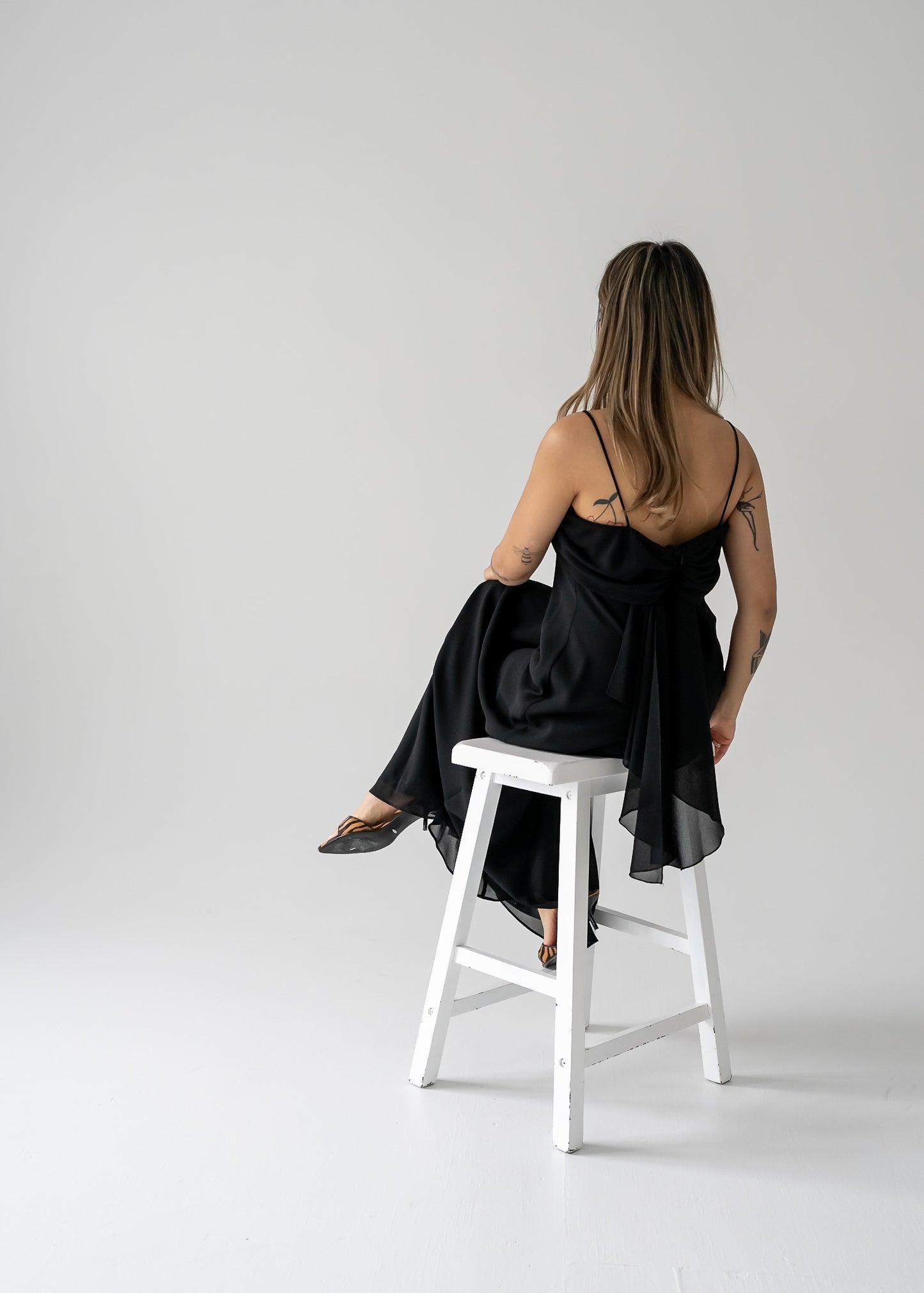 Person sitting on a white stool wearing a black dress in a studio setting.