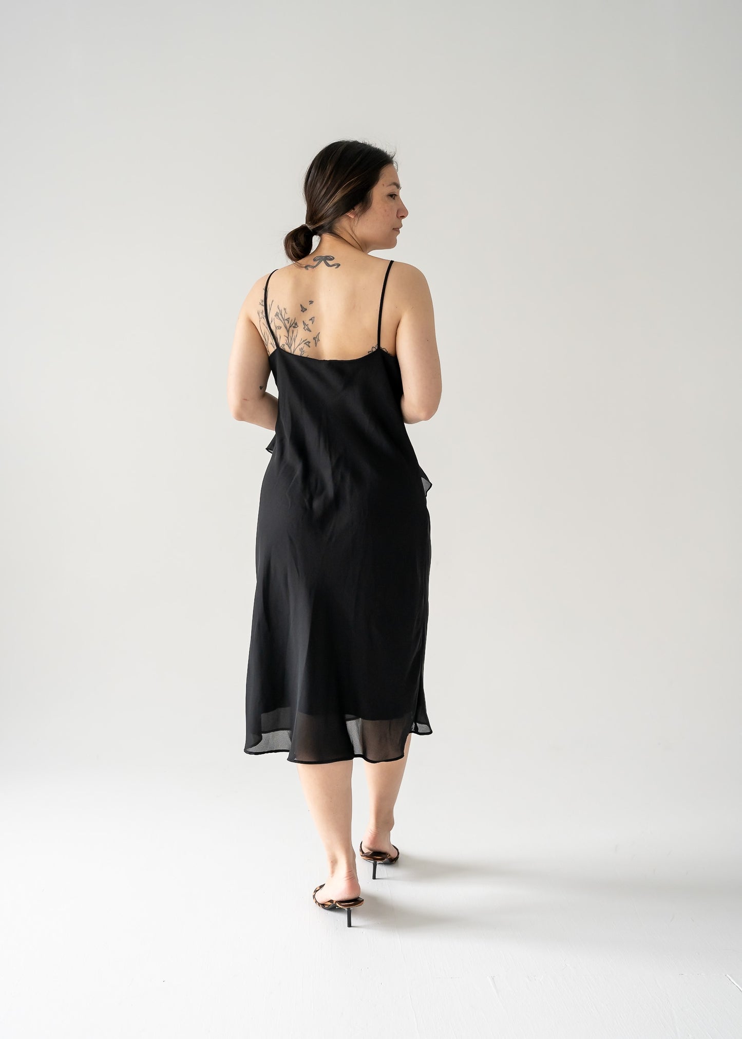 A model wearing a vintage black spaghetti strap bias ruffle midi dress with a V-neck and flat hem.
