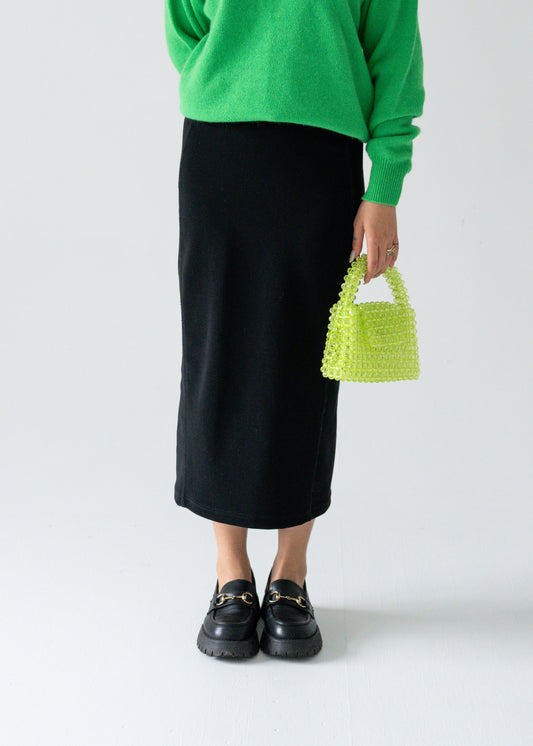 A person wearing a green sweater and a vintage black column midi skirt with a lime green handbag and black shoes.