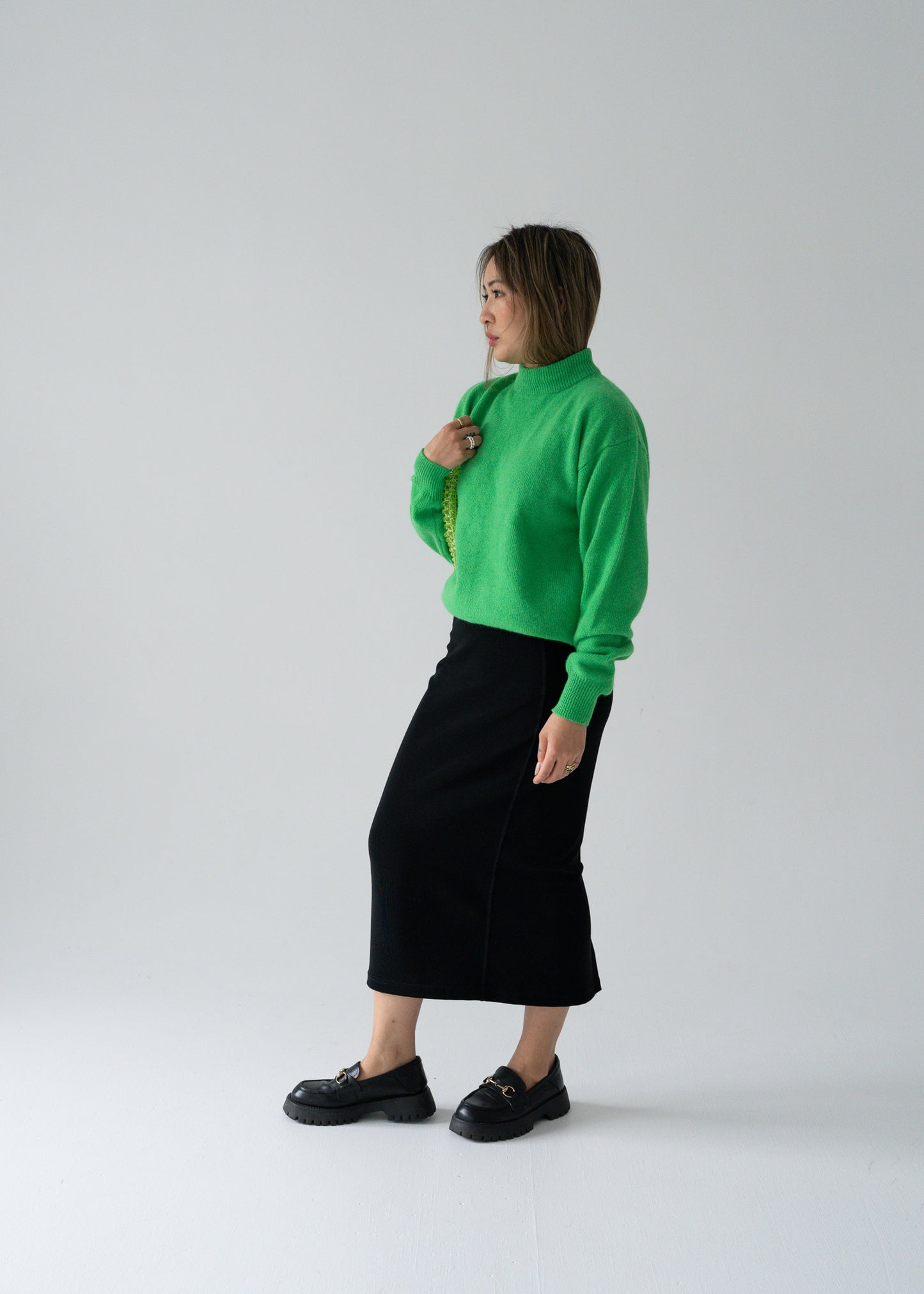 Person wearing a bright green angora sweater and vintage black column black skirt on a light background
