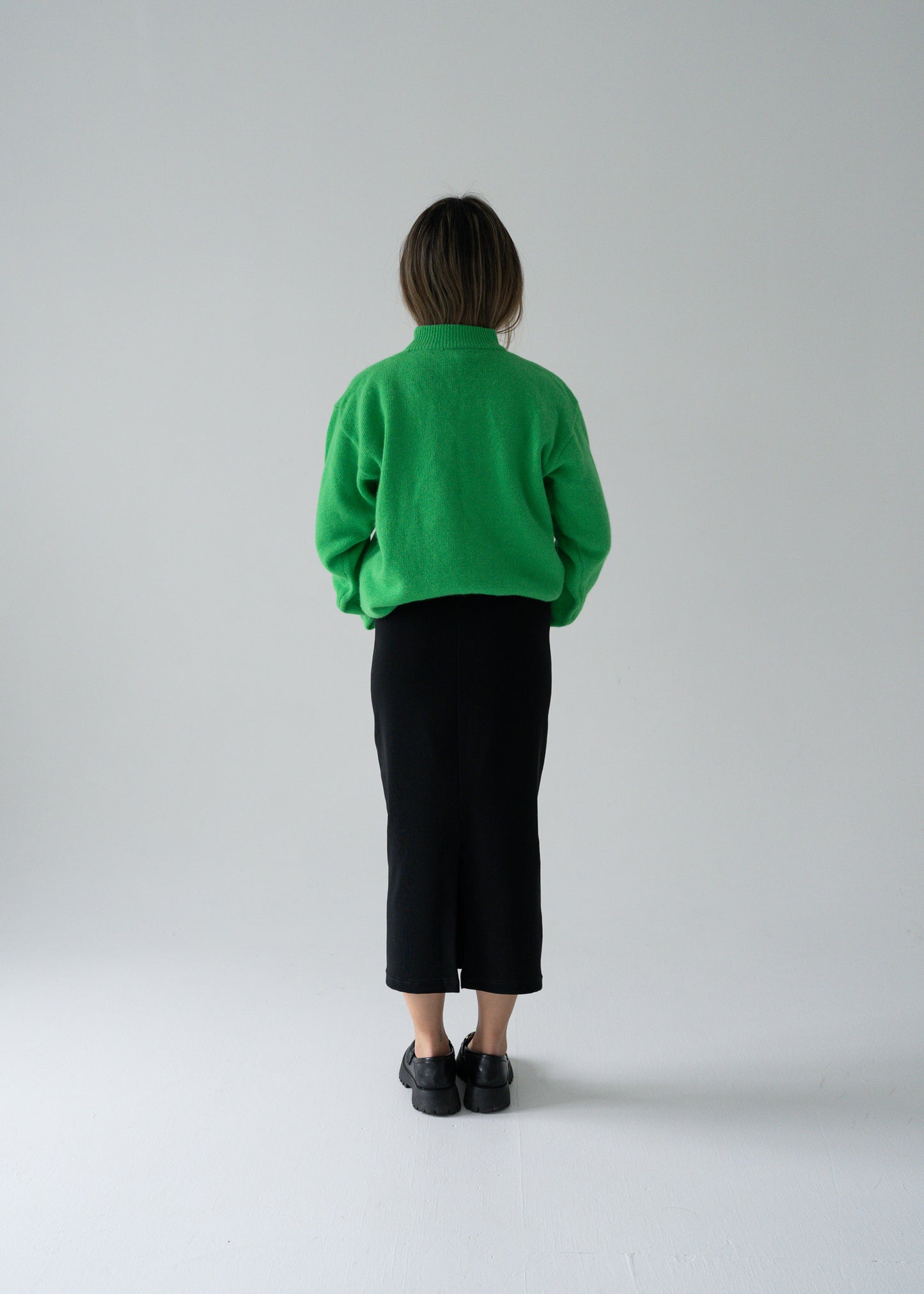 Person wearing a green angora sweater and vintage black skirt against a plain background
