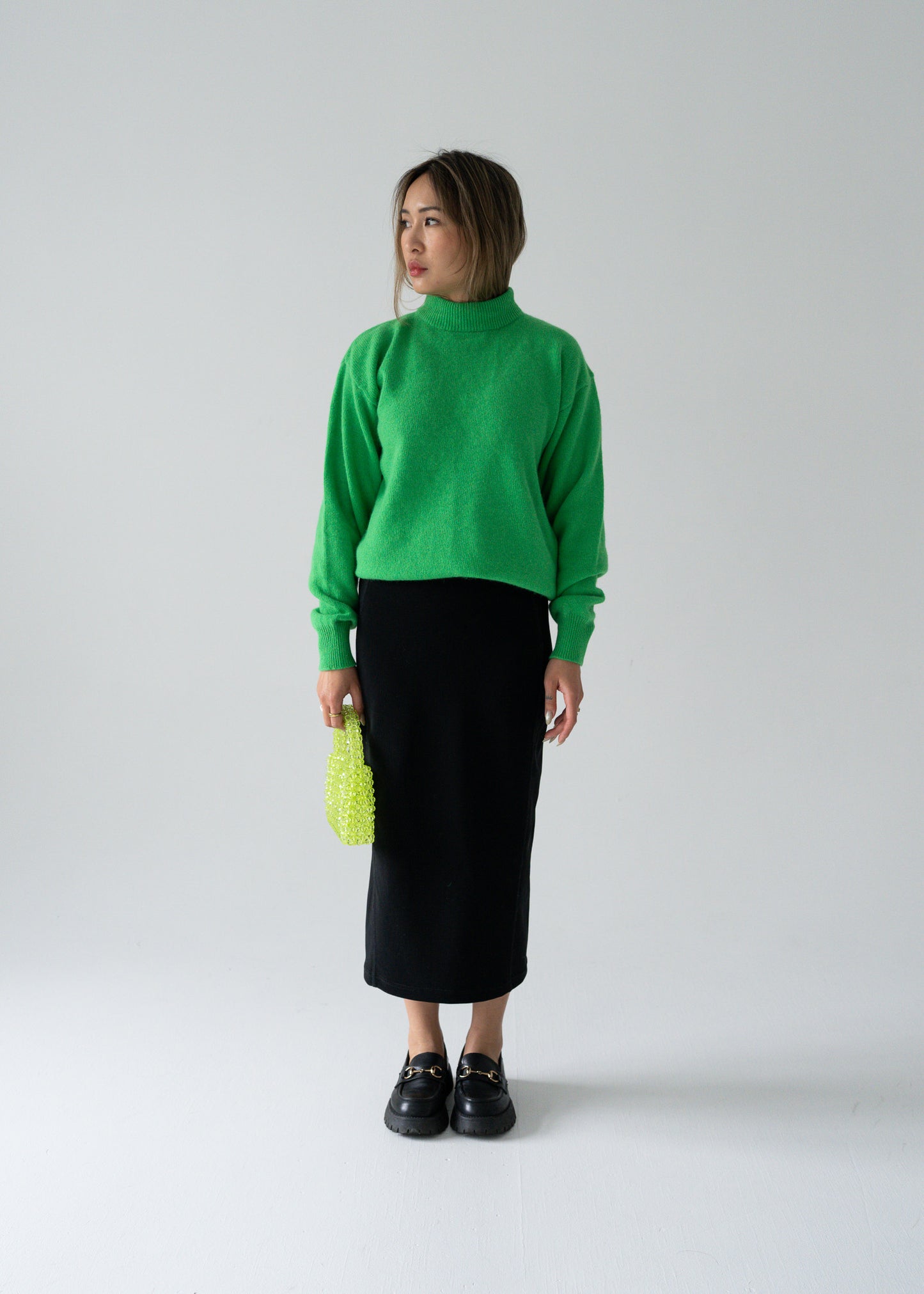 Person wearing a vintage green angora sweater and vintage black column skirt on a neutral background