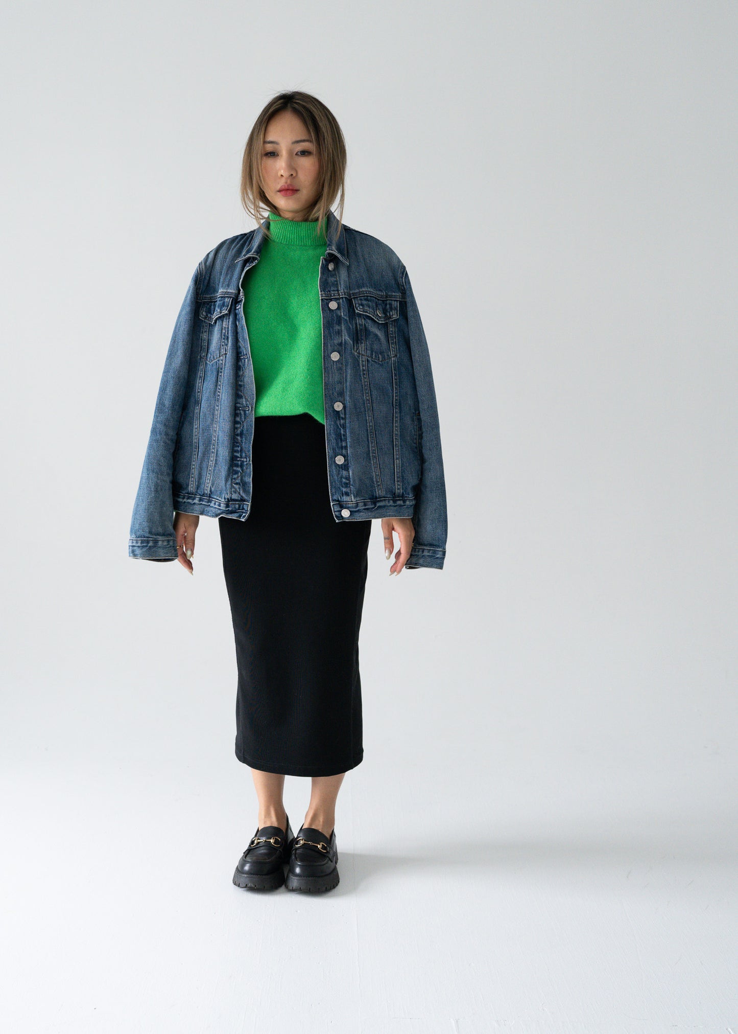 Person wearing a denim jacket, green sweater, and vintage black skirt on a white background