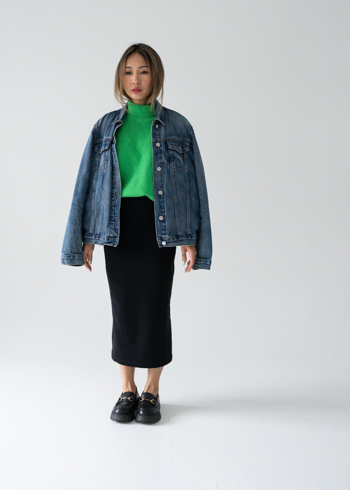 Person wearing a denim jacket, green sweater, and vintage black skirt on a white background