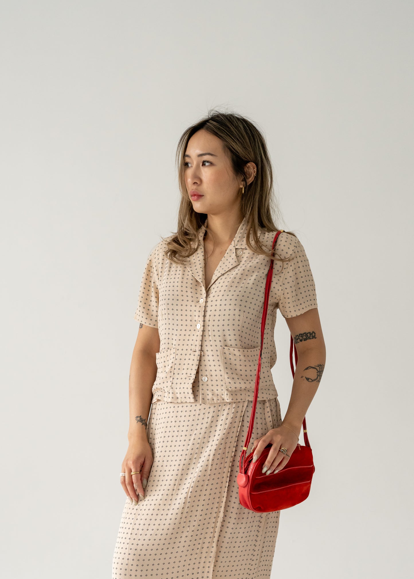 A person wearing a dotted dress  holding a vintage strawberry red suede leather crossbody bag with small gold hardware.
