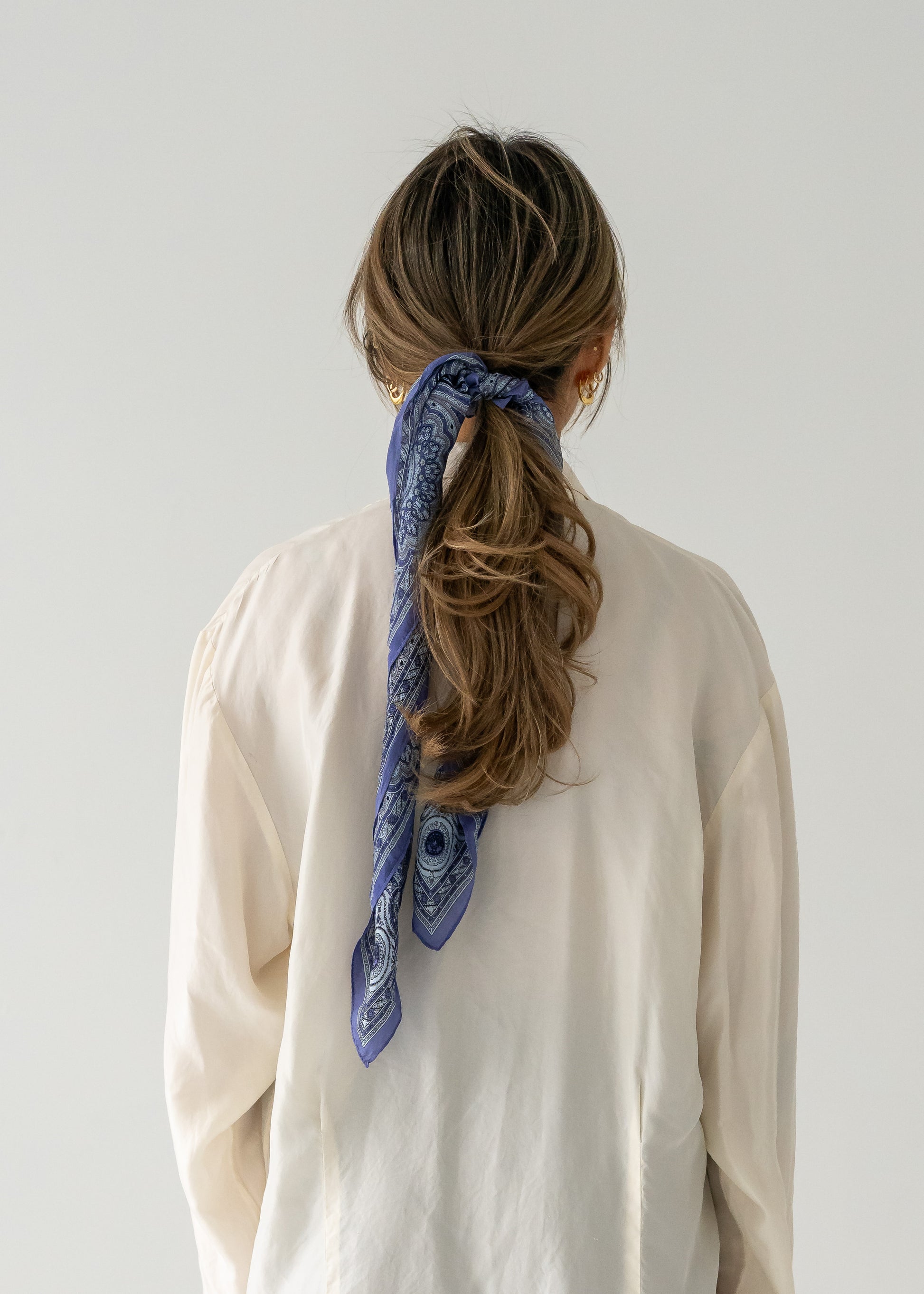 A person viewed from the back wearing a multi purple and blue paisley silk scarf tied in their hair.