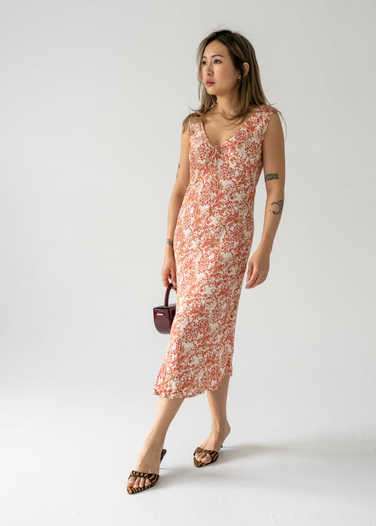 A model wearing a vintage sleeveless, cream and pink floral print midi dress with a cinch top, standing against a plain background.