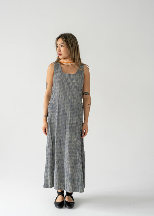 A model wearing a vintage sleeveless, knee-length, checkered dress in blue and cream colors with side button details.