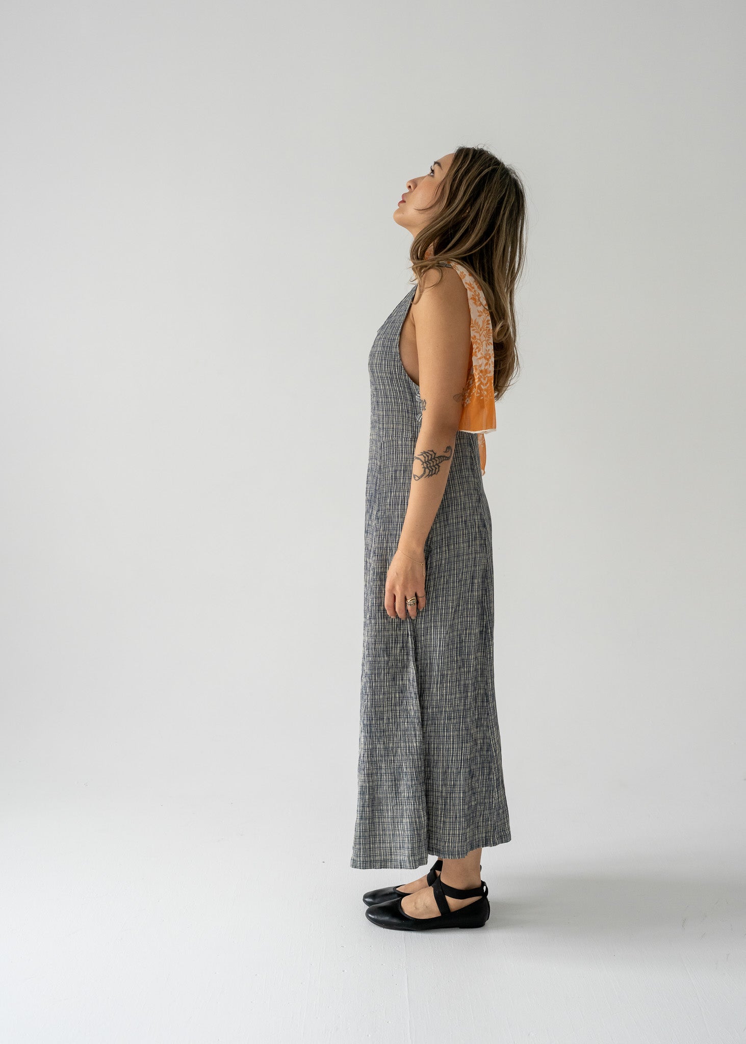 Woman in a vintage sleeveless, knee-length, checkered dress in blue and cream colors looking to the side on a white background