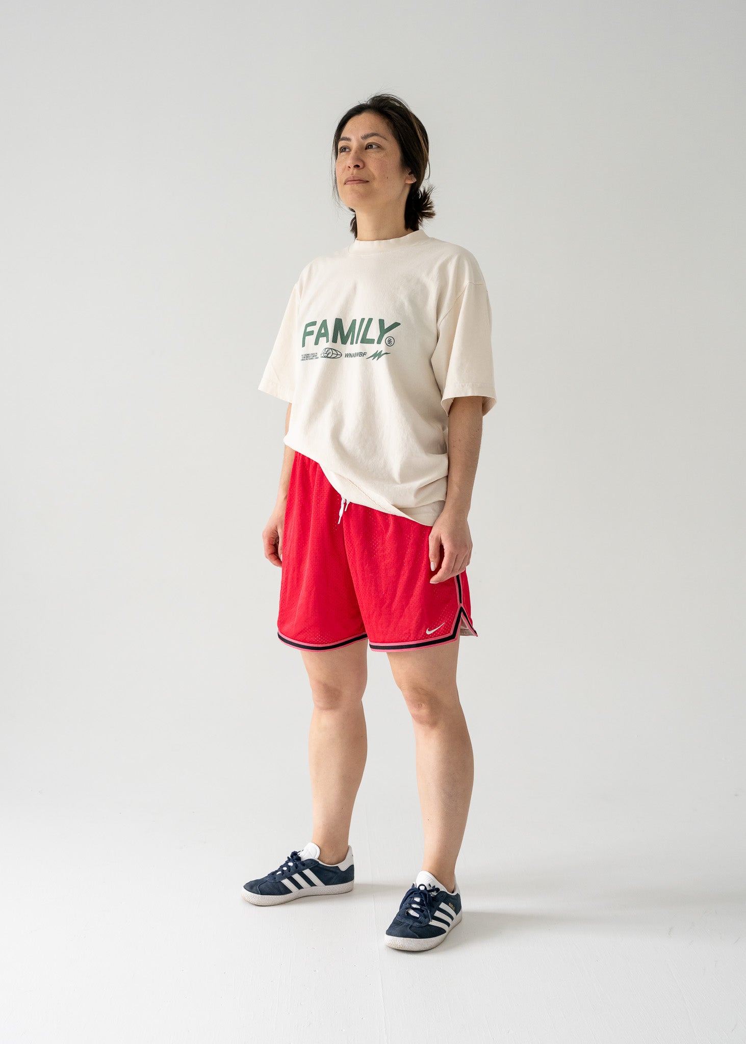 Person wearing a white t-shirt with 'FAMILY' text and vintage red mesh Nike shorts with black side stripes on a plain background.