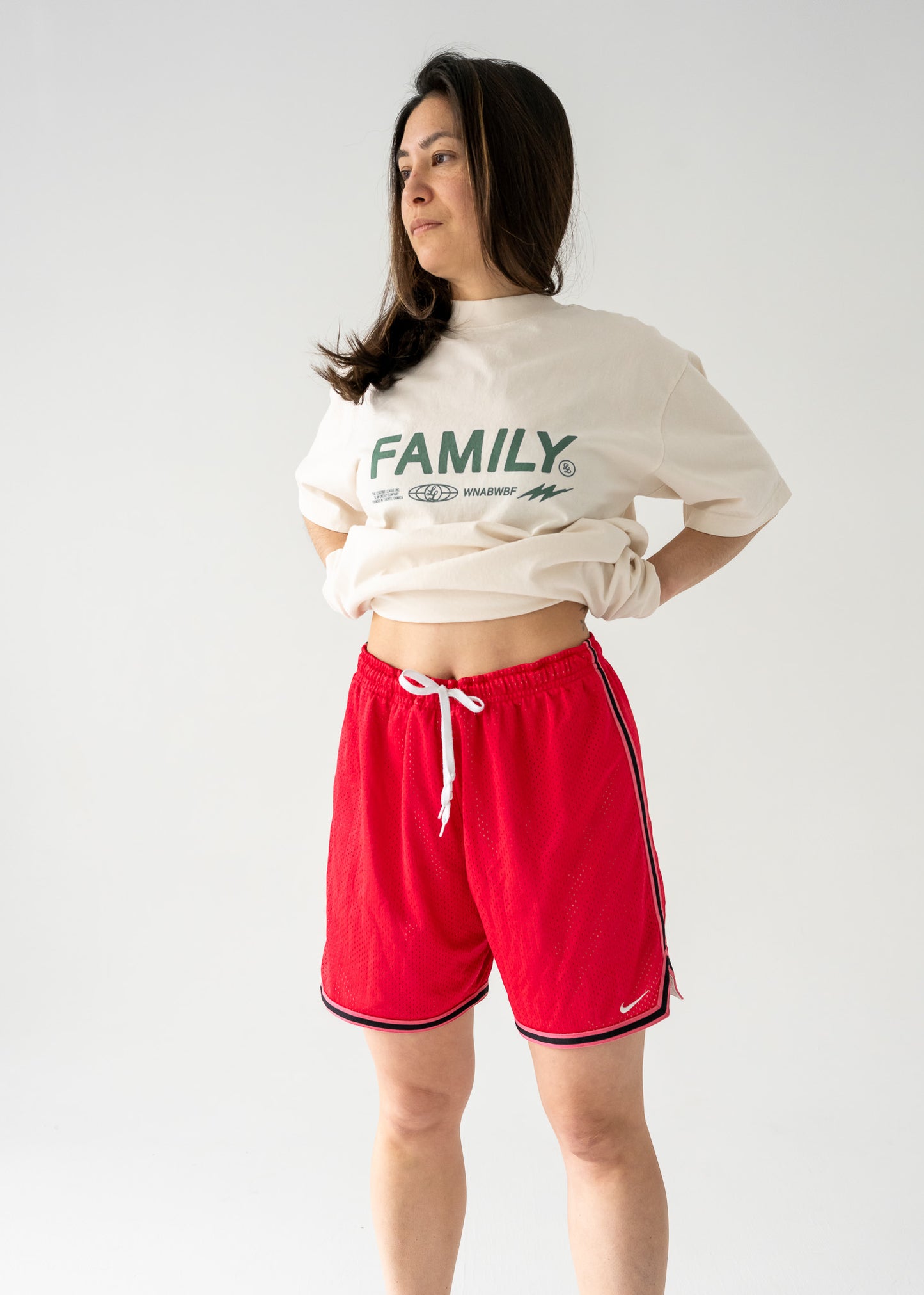 Person wearing a cropped white shirt and vintage red mesh Nike shorts with black side stripes on a plain background