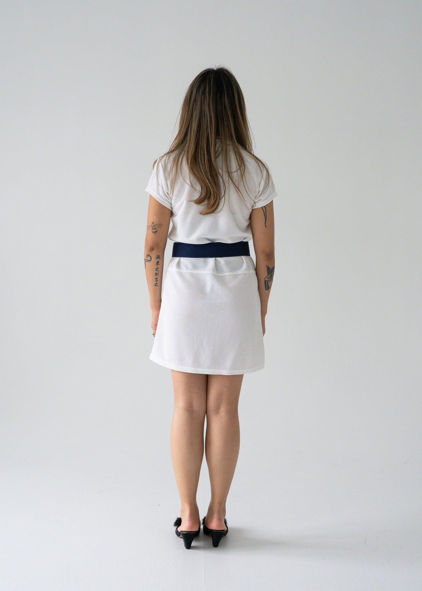 Person wearing a white dress with a navy belt on a gray background
