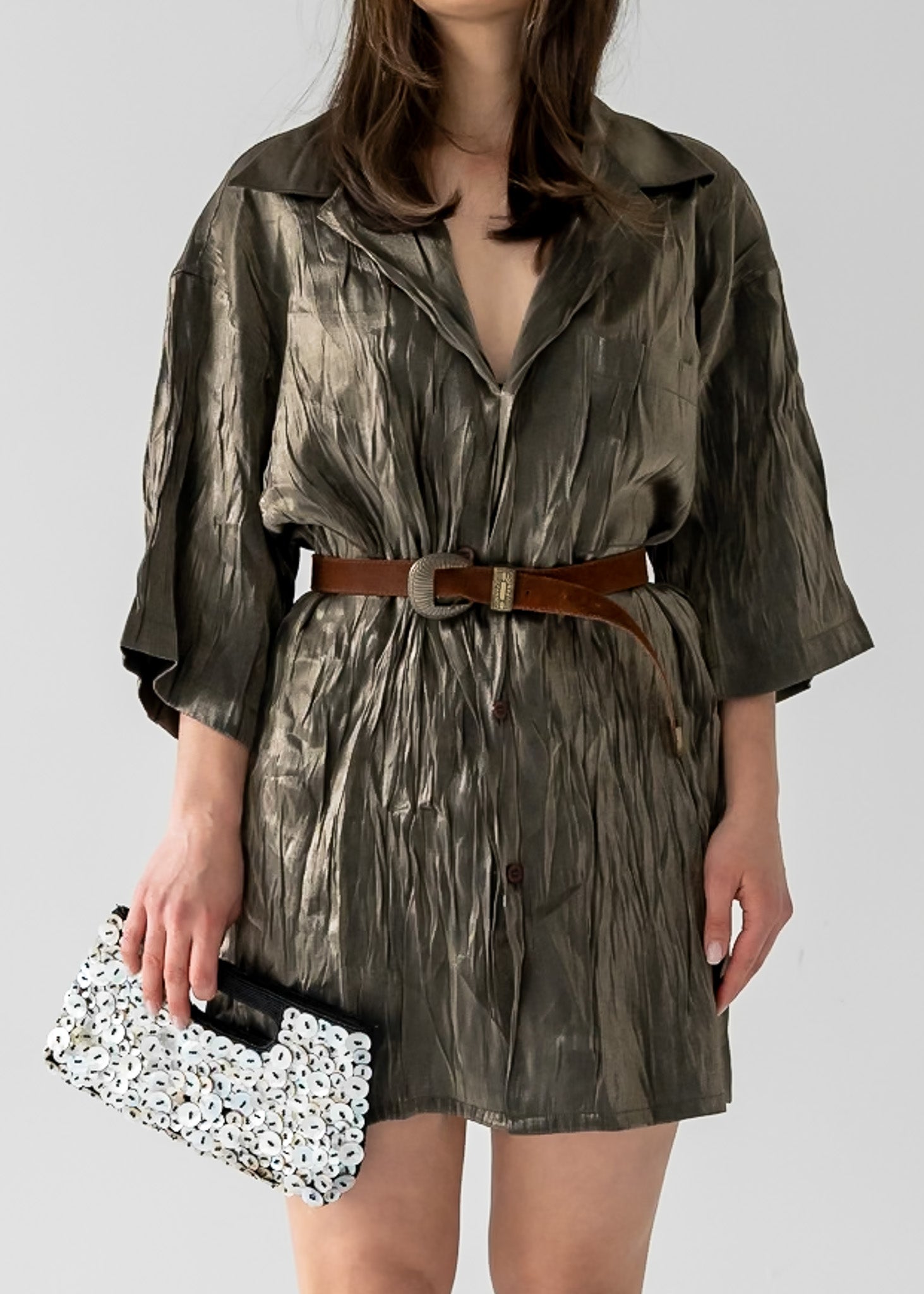 Person wearing a green patterned dress with a brown suede belt with a decorative buckle, holding a black and white shell clutch.