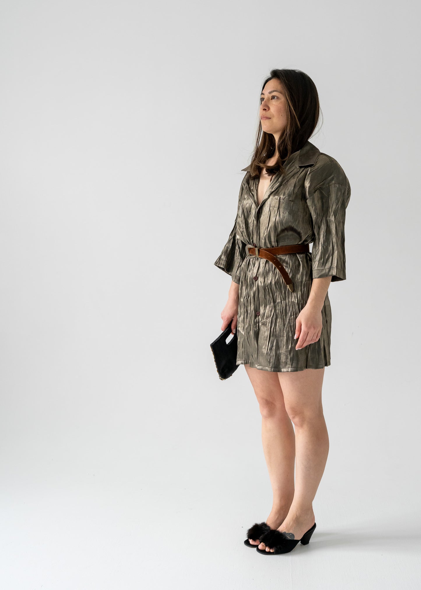 A woman standing in a side profile pose wearing a vintage green bronze full sheen textured lightweight short sleeve button up mini dress with a collared neck.