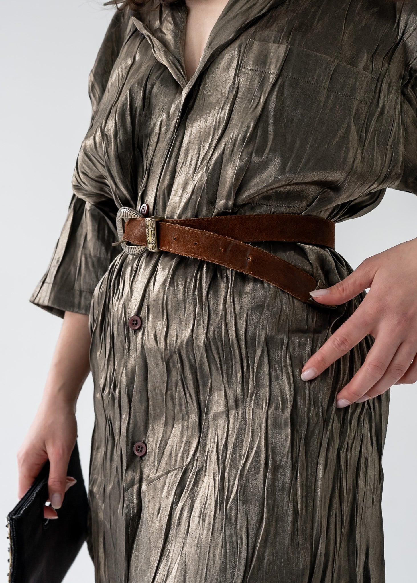 A woman standing in a side profile pose wearing a vintage green bronze full sheen textured lightweight short sleeve button up mini dress with a collared neck with a brown suede belt. 