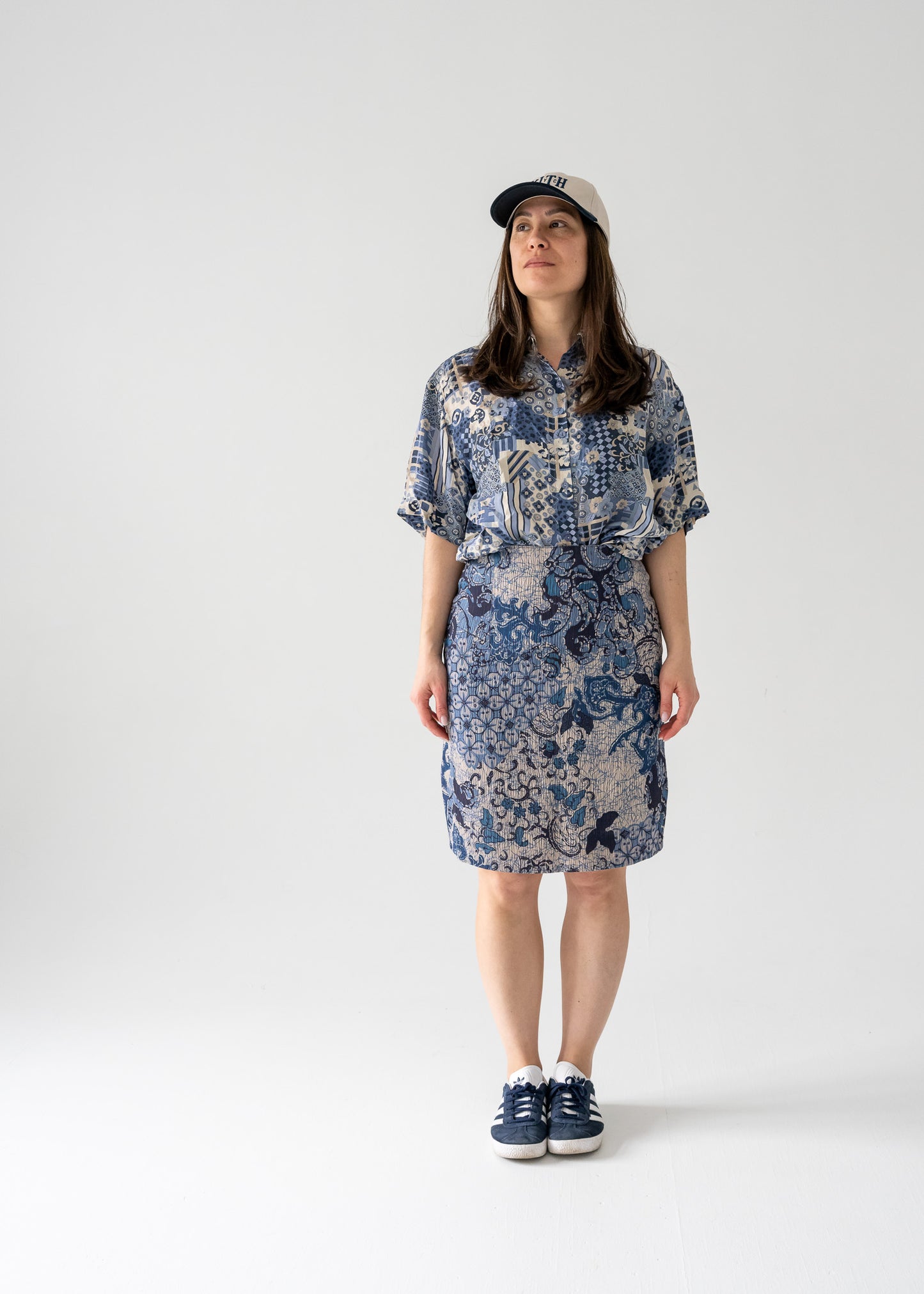 A model wearing a vintage knee-length blue floral pattern pencil skirt with a cap and sneakers.