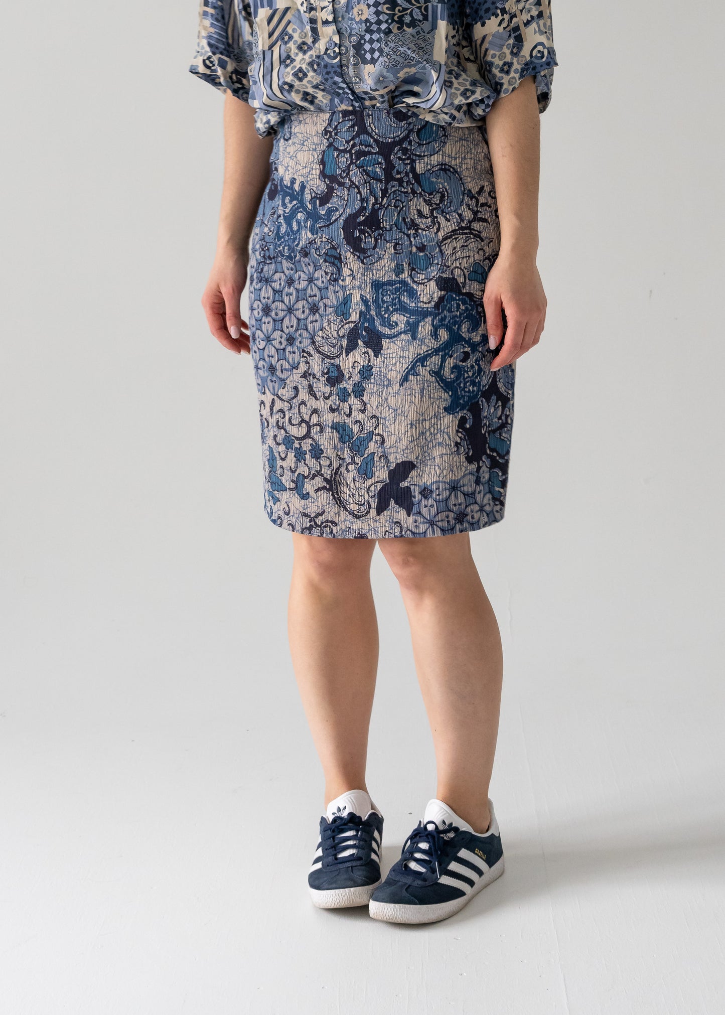 Person wearing a knee-length blue floral pattern vintage pencil skirt and sneakers on a white background