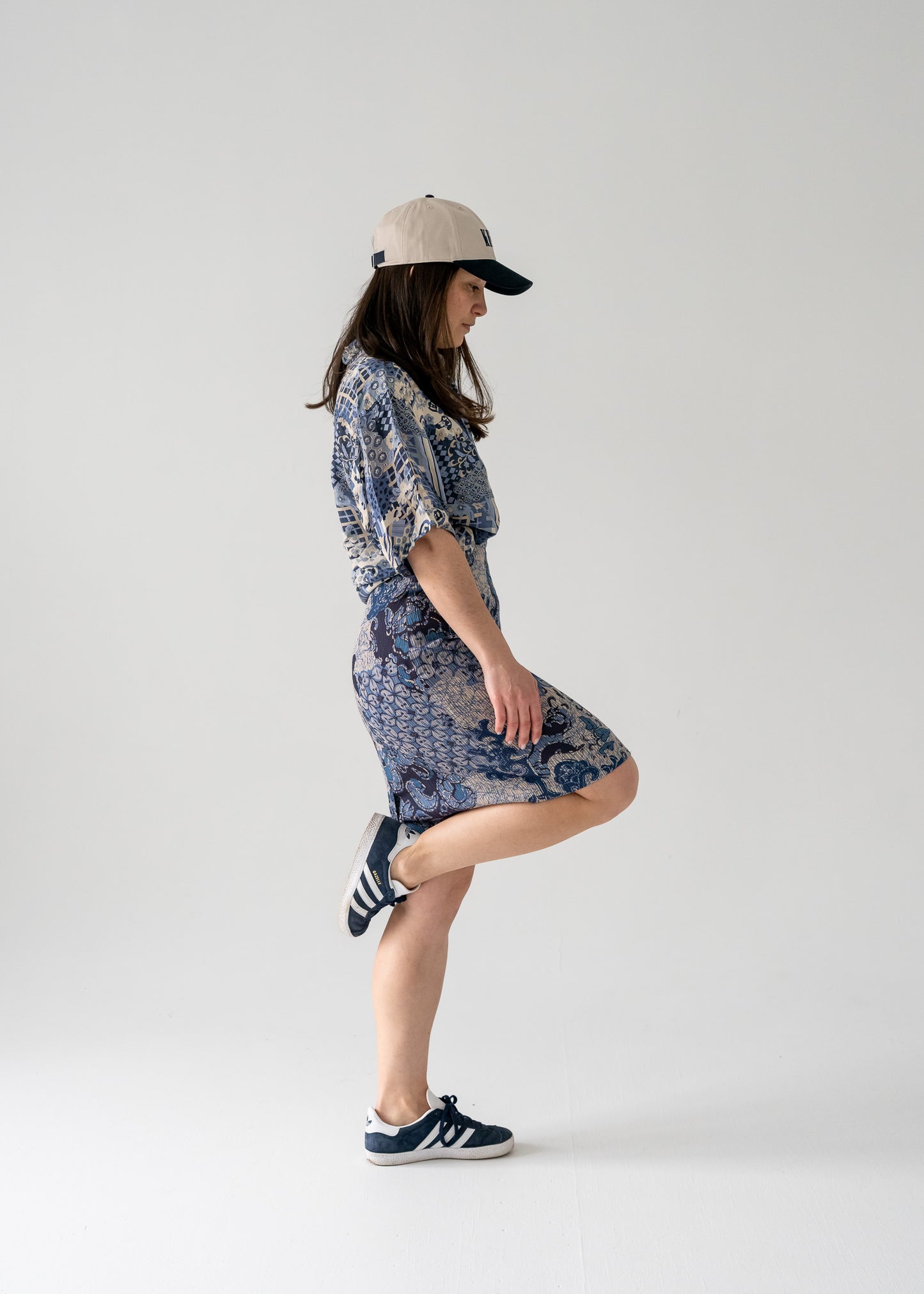 Woman in a knee-length blue floral pattern vintage pencil skirt and matching vintage silk shirt and cap posing against a plain background.
