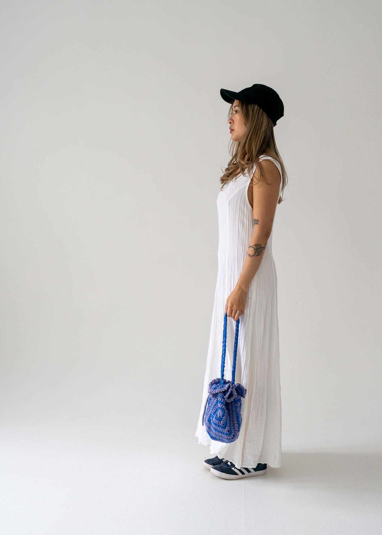 Person wearing a vintage ivory crinkle lightweight floor-length princess seam sleeveless dress holding a blue bag against a plain background