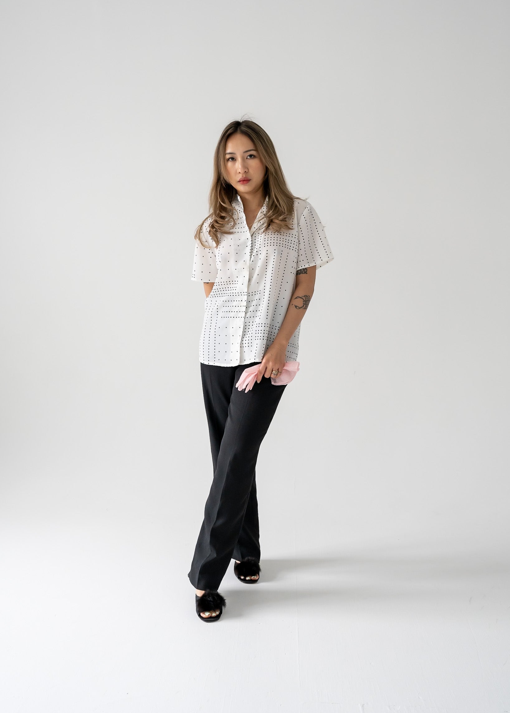 A woman wearing a vintage white short sleeve button up blouse with black square polka dots, paired with black pants.
