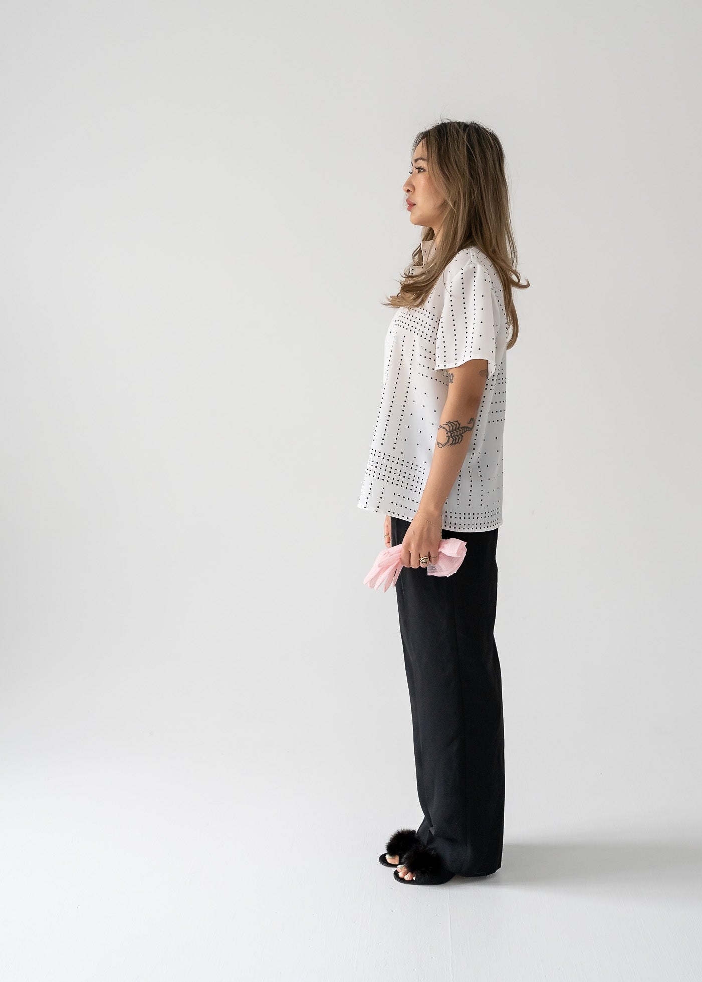 A woman wearing a vintage white short sleeve button up blouse with black square polka dots, paired with black pants.