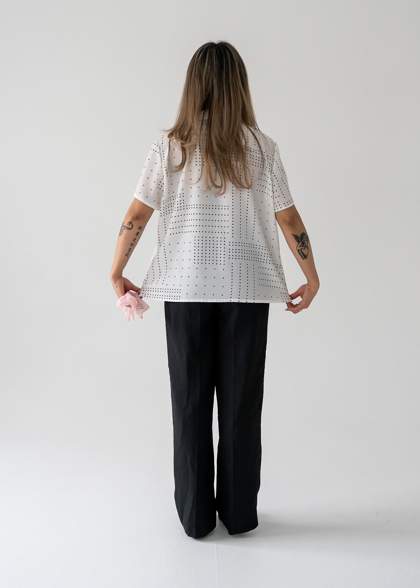 A woman wearing a vintage white short sleeve button up blouse with black square polka dots, paired with black pants.
