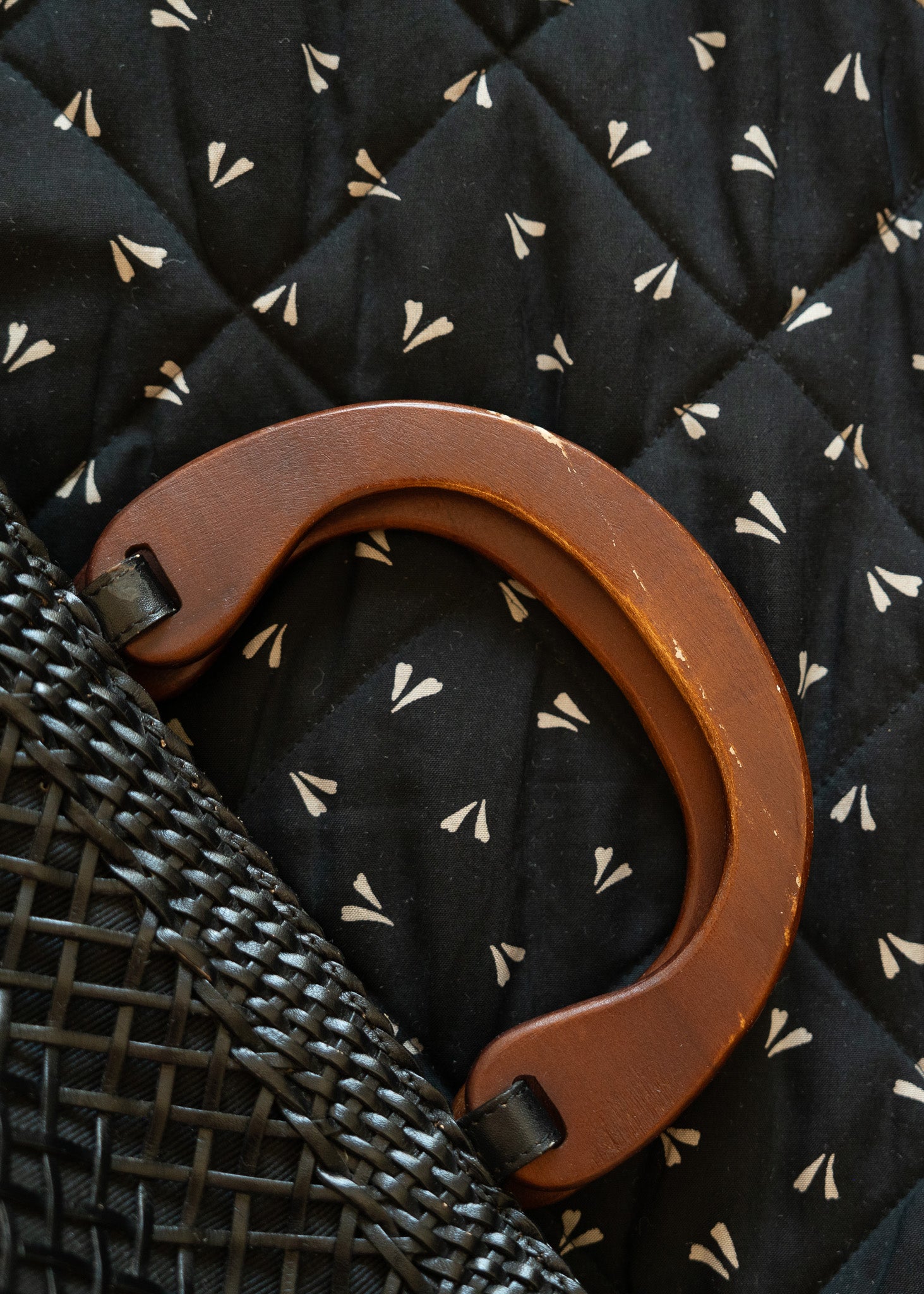 detail shot of a vintage black leather handbag with an open basket weave pattern and wooden handles  against a black background