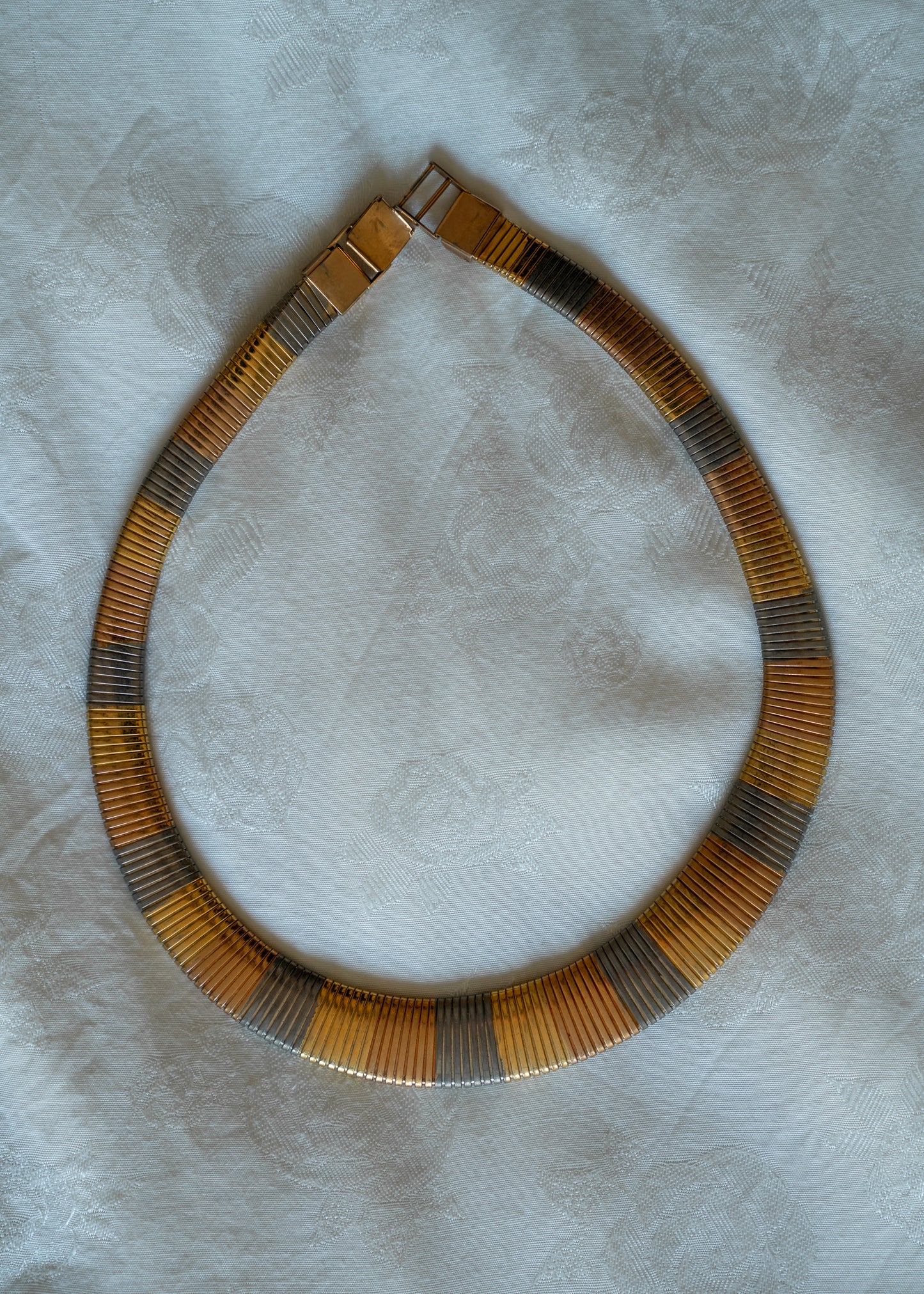 Multi-metal choker necklace on a textured white surface