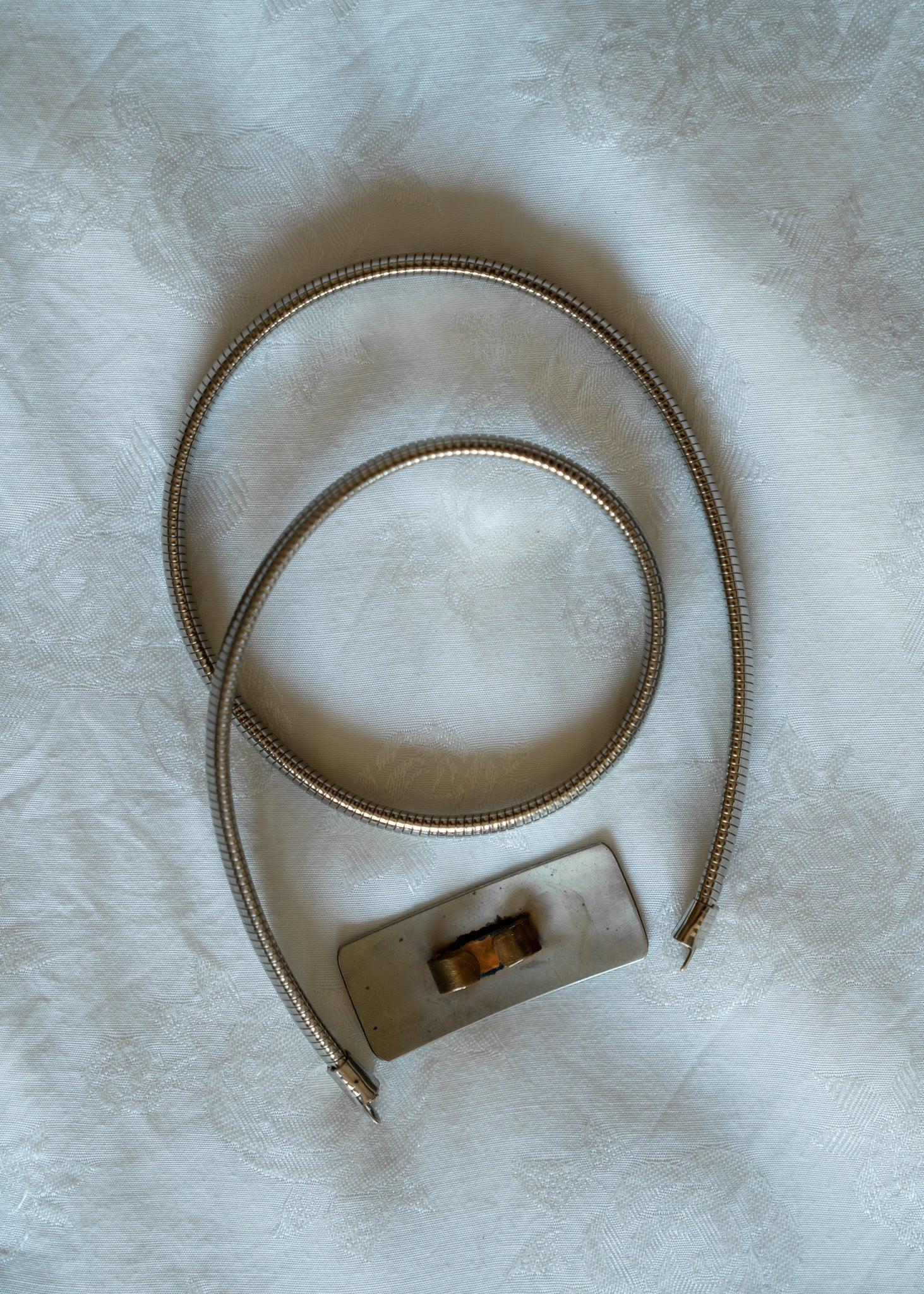 Silver metal belt with a silver buckle on a light gray background
