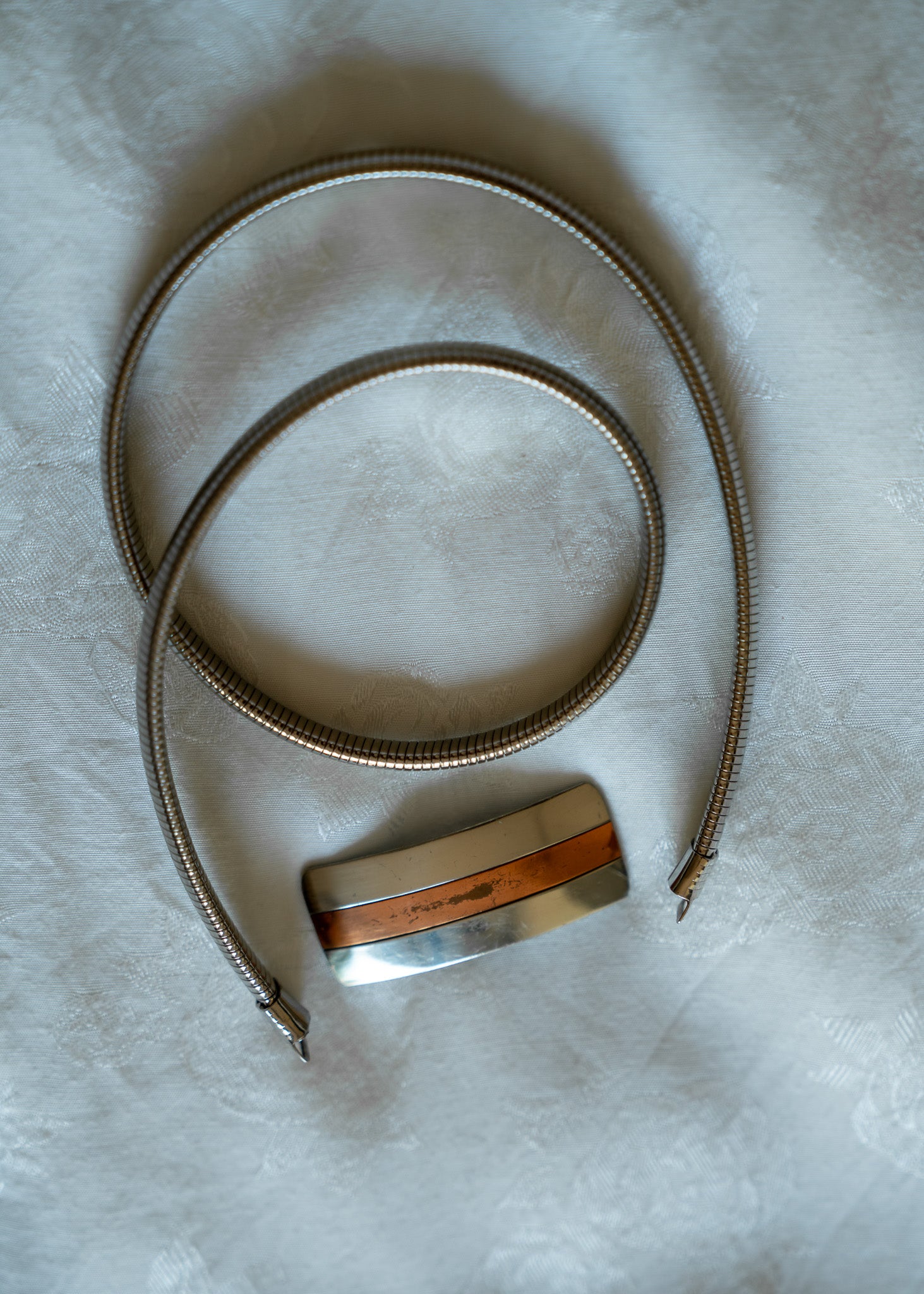 Silver and copper metal belt with a rectangular buckle on a light fabric background