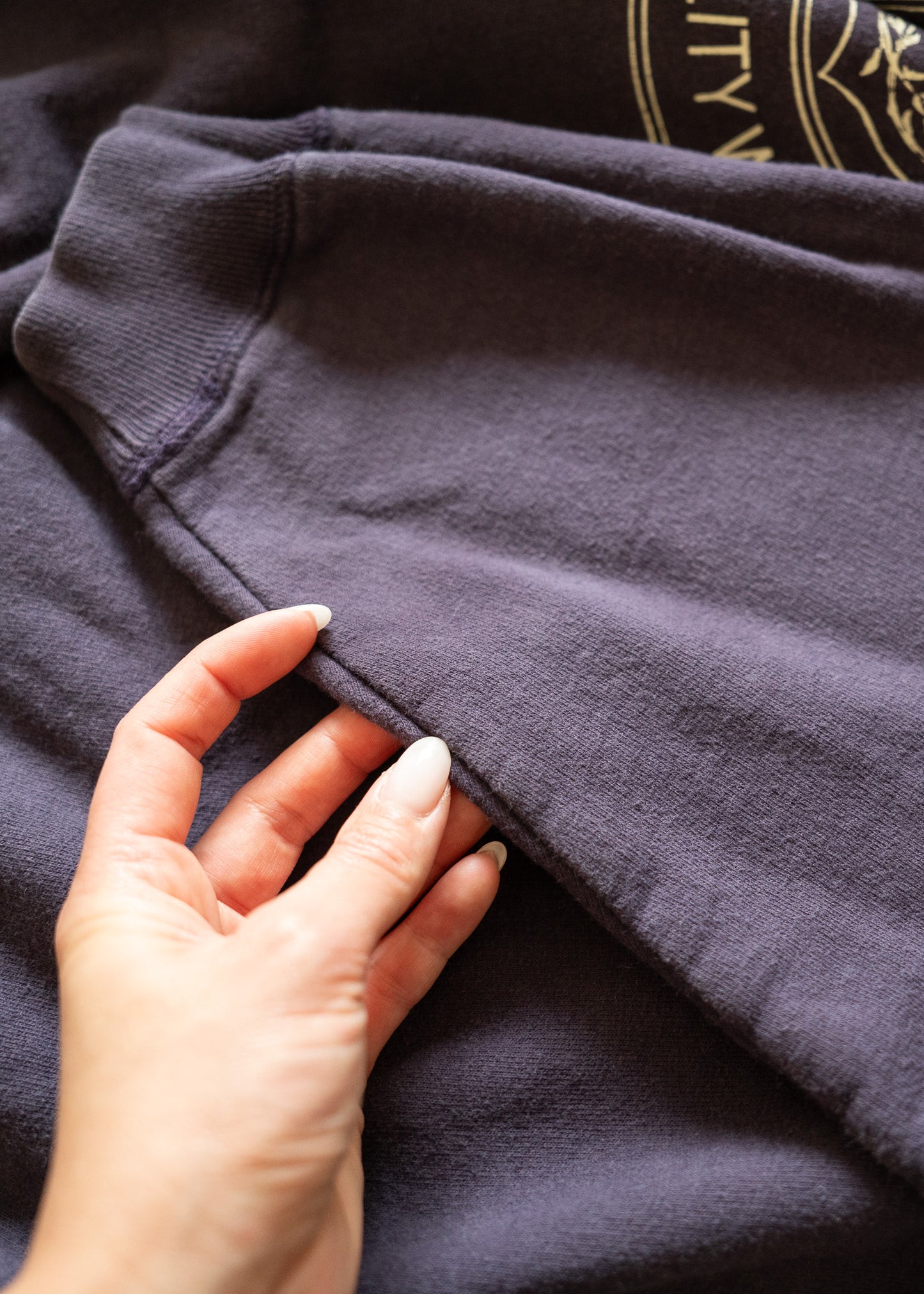 Hand touching a dark purple fabric with a brand logo in the corner