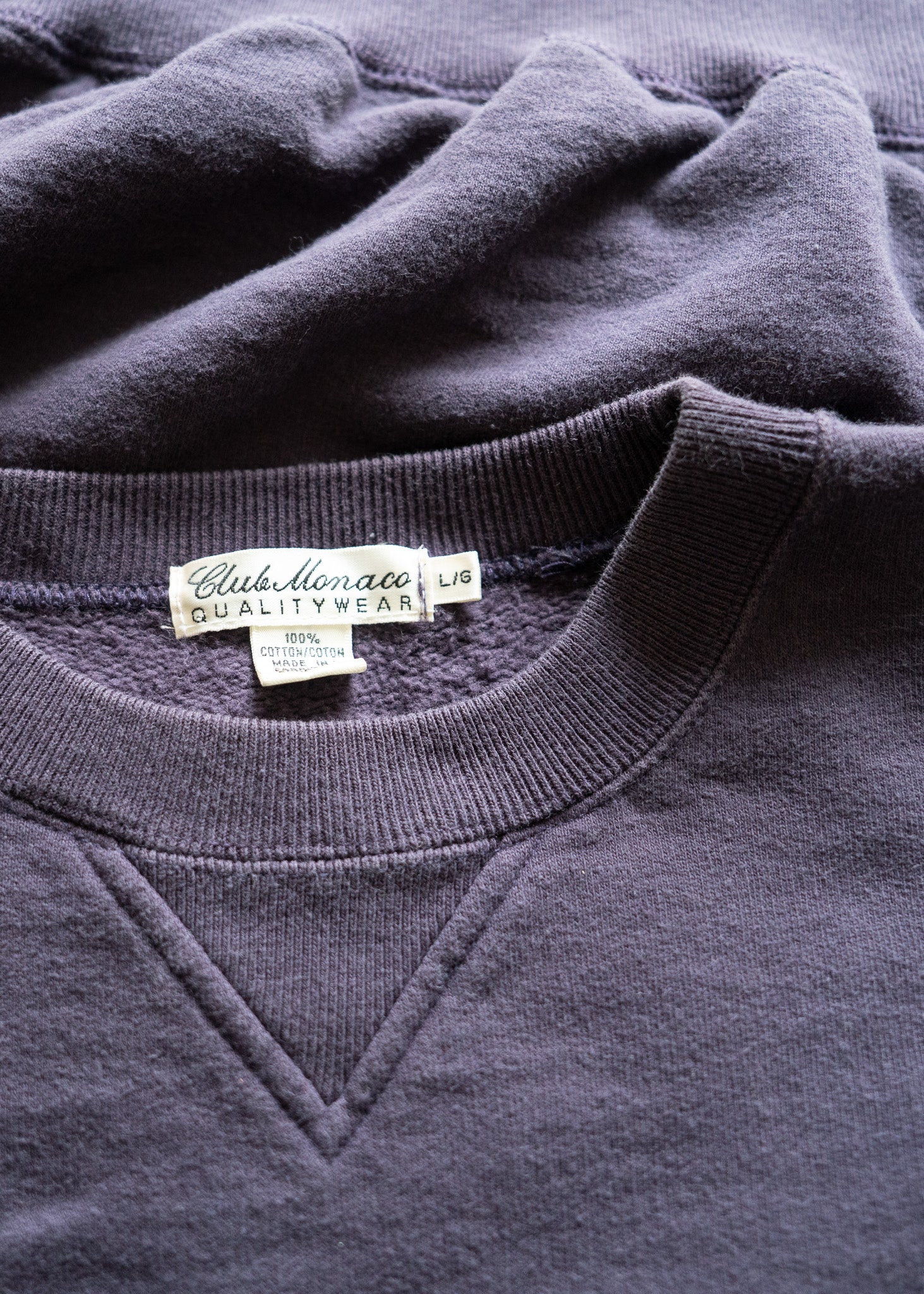 Close-up of a dark purple sweatshirt with a vintage Club Monaco label on the collar.