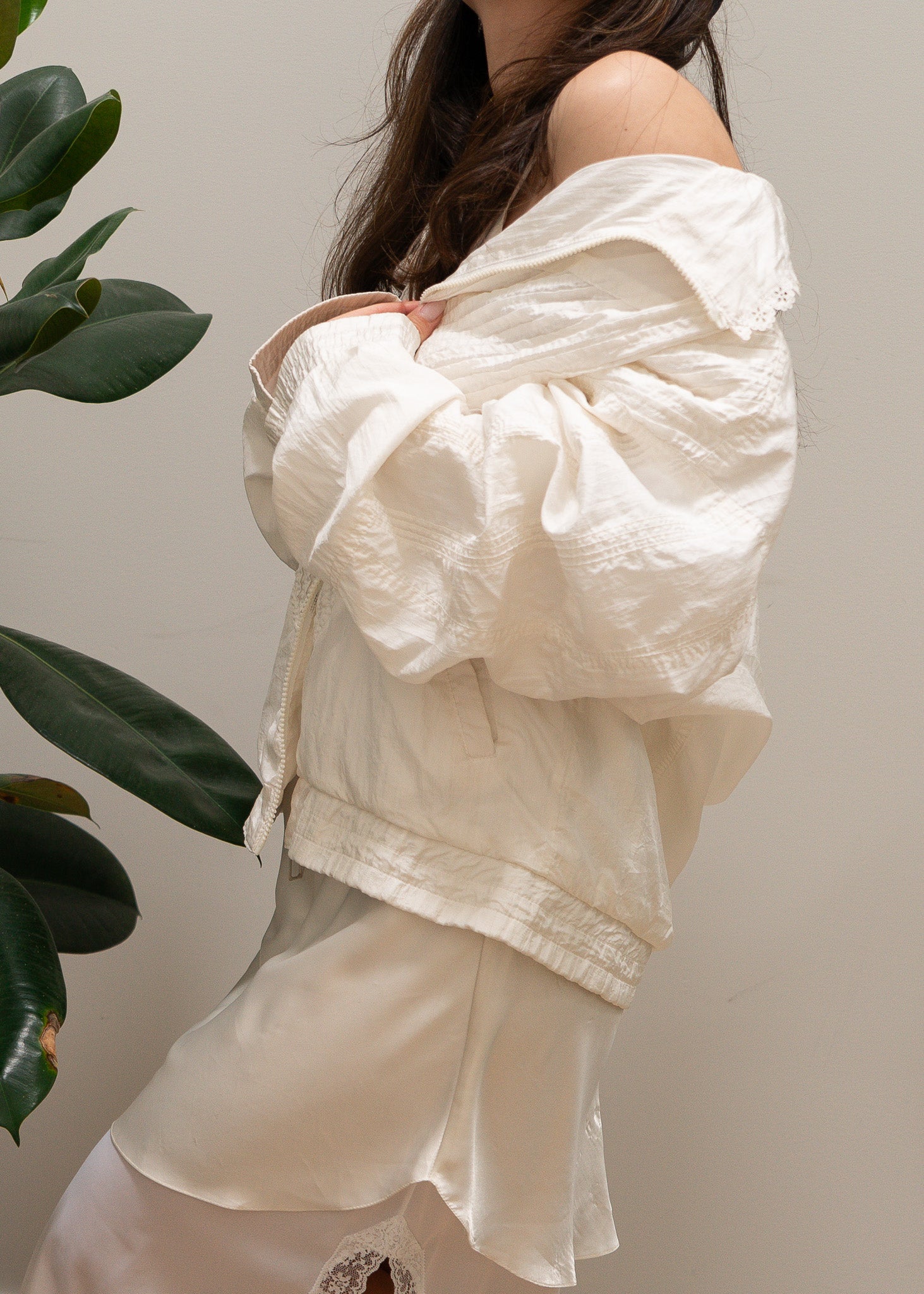 Person wearing a white off-shoulder jacket and satin slip with a neutral background
