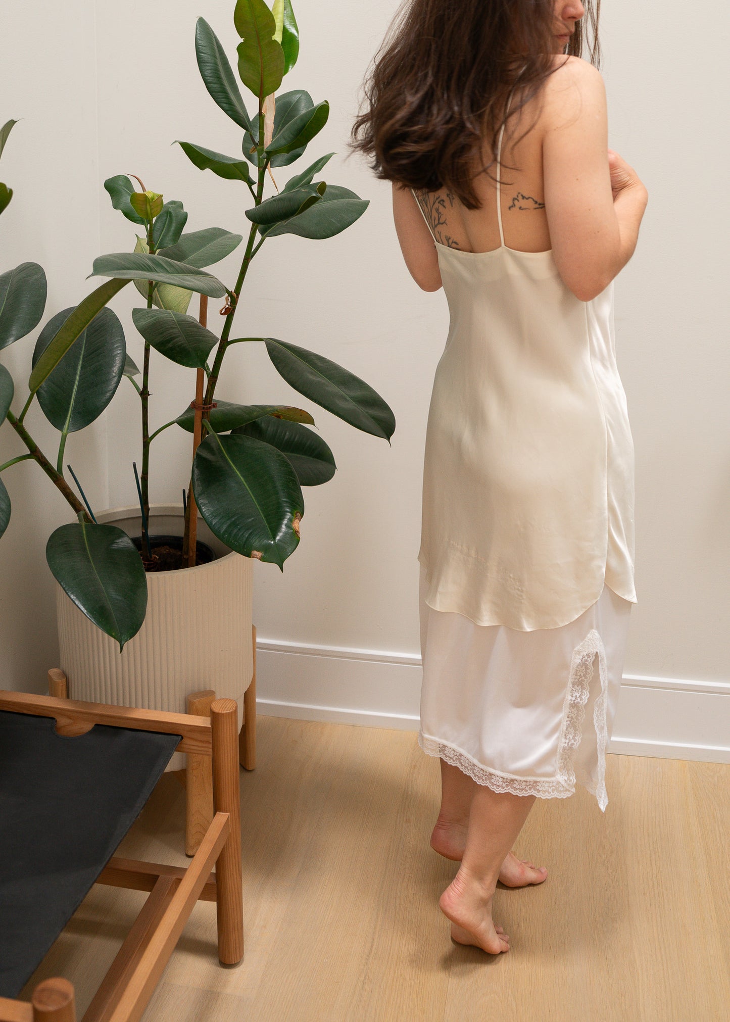 Woman in a white slip standing next to a potted plant indoors