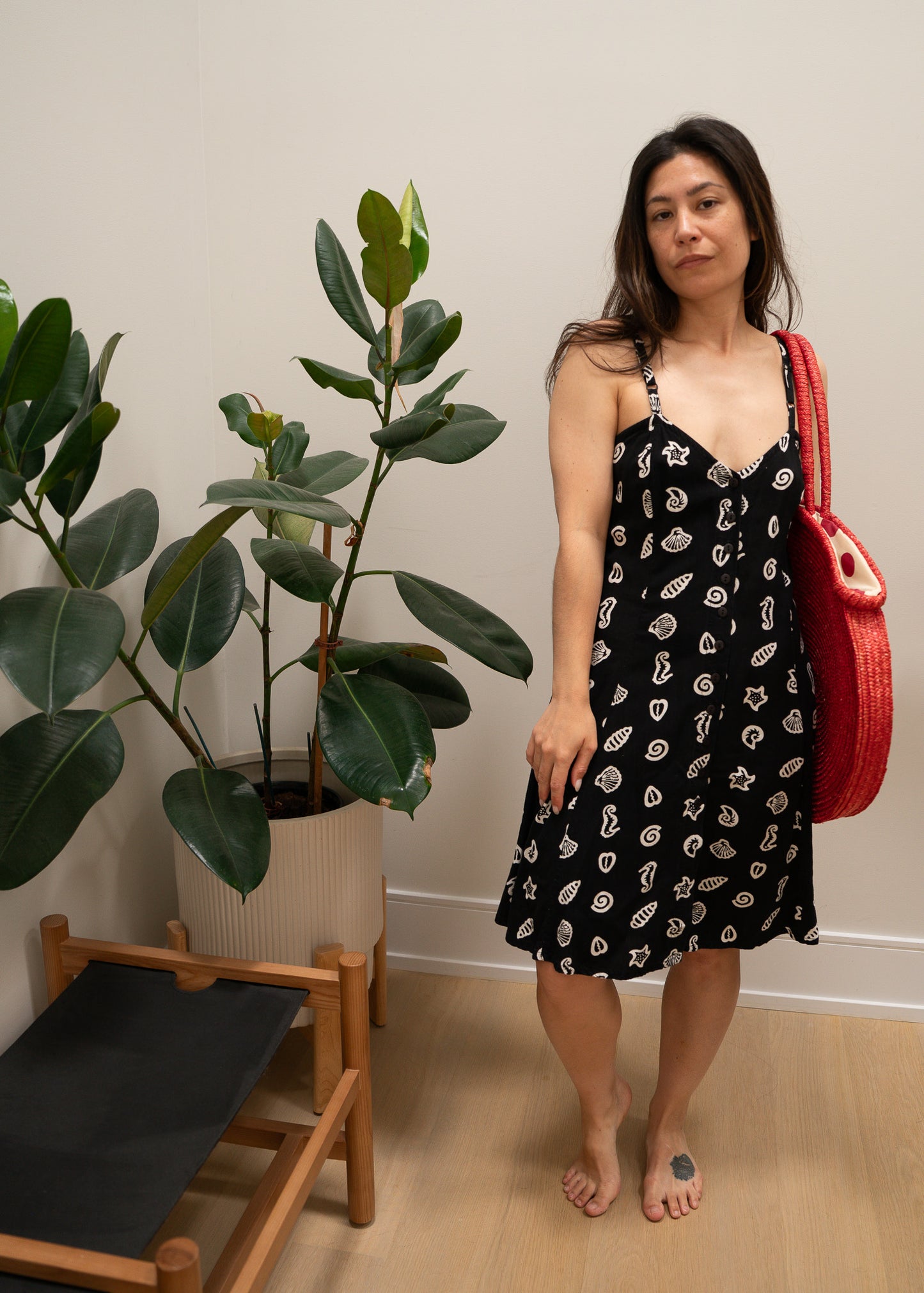 Woman in a black dress with white ocean patterns holding a red bag indoors.