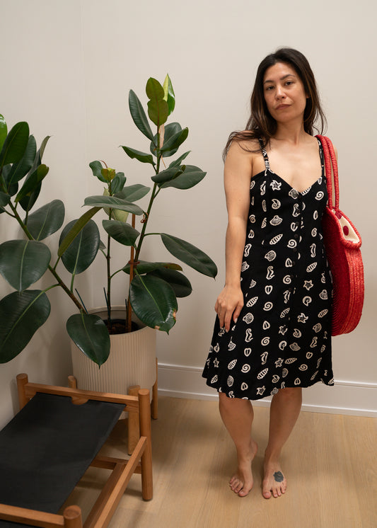 Woman in a black dress with white ocean patterns holding a red bag indoors.
