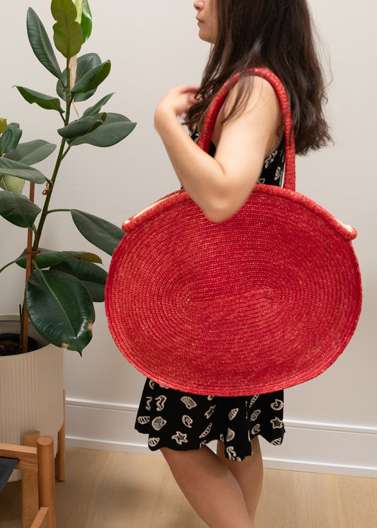 Person holding a large red woven bag indoors with a plant in the background