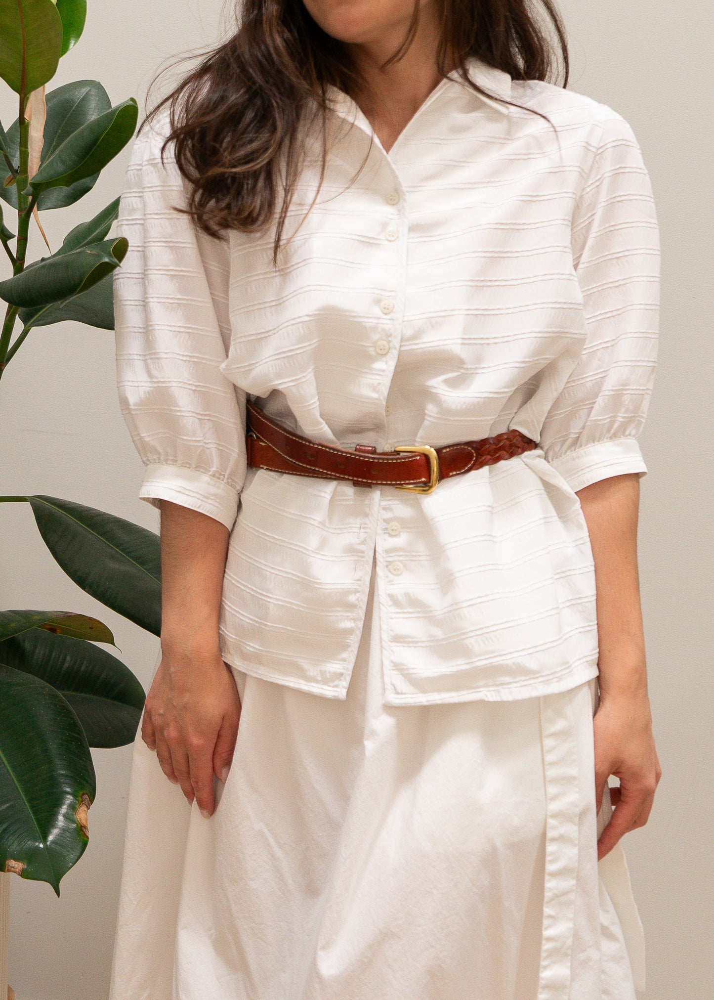 Person wearing a white white striped puffy sleeve blouse and white skirt with a brown belt against a neutral background
