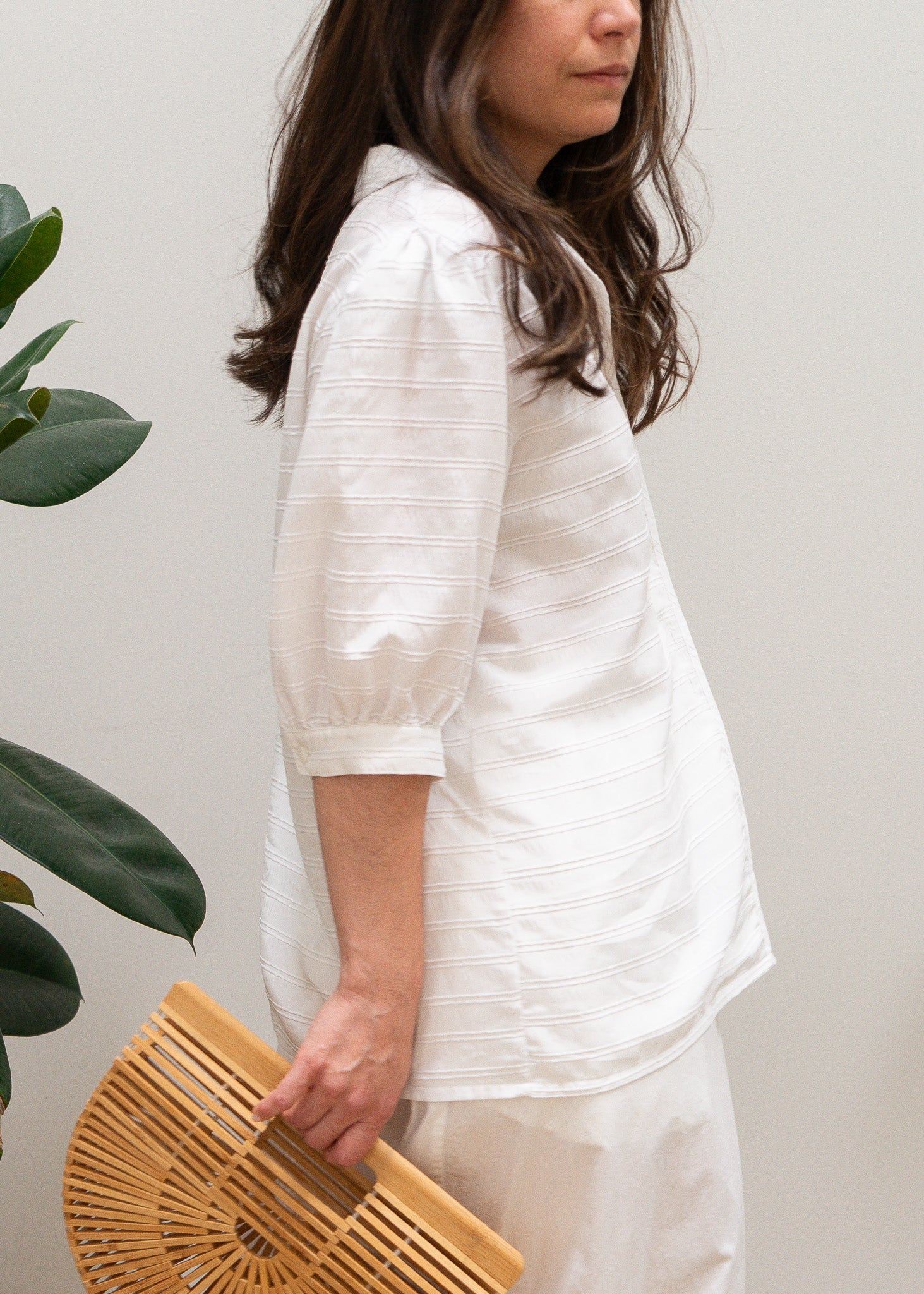 Person wearing a white white striped puffy sleeve blouse holding a wooden clutch against a plain background
