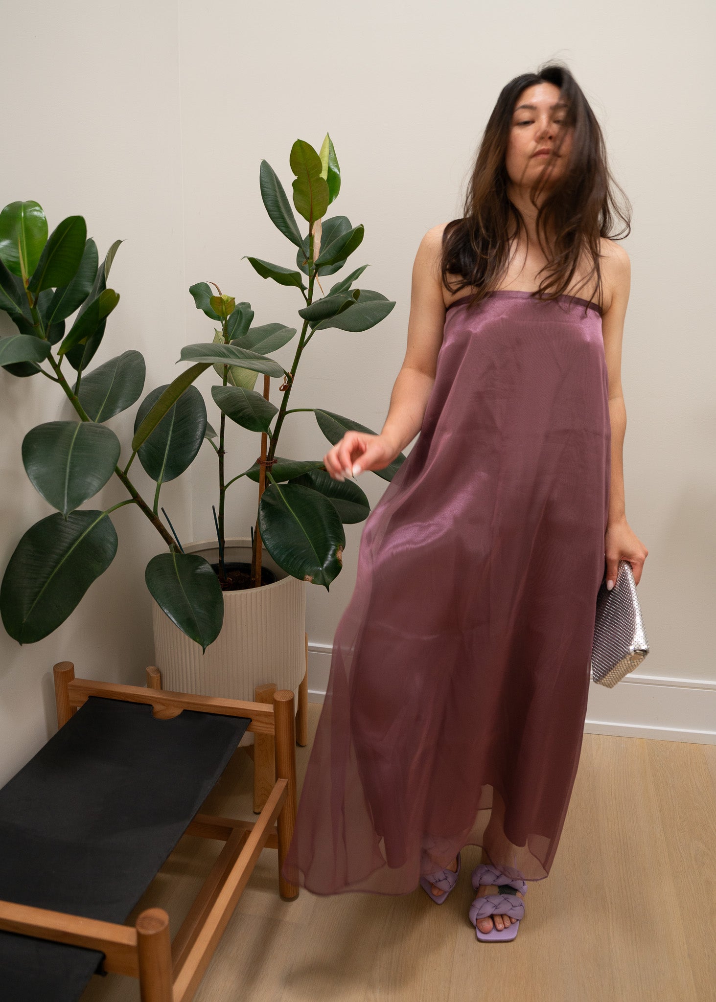 Woman in a strapless mauve purple dress standing next to a plant indoors