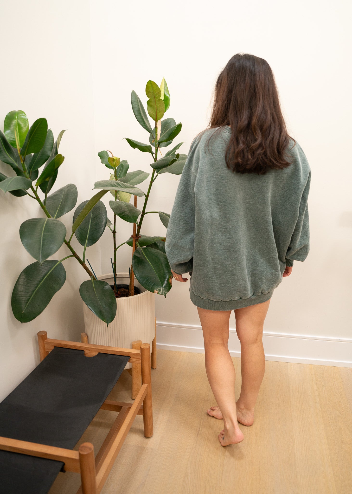 Person in a green sweatshirt standing next to a potted plant indoors.