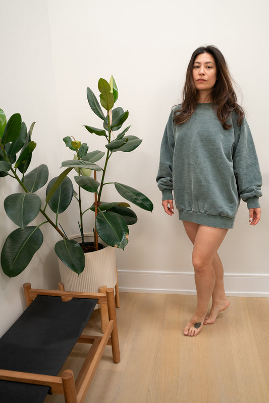 Woman in a green sweater standing next to a plant indoors