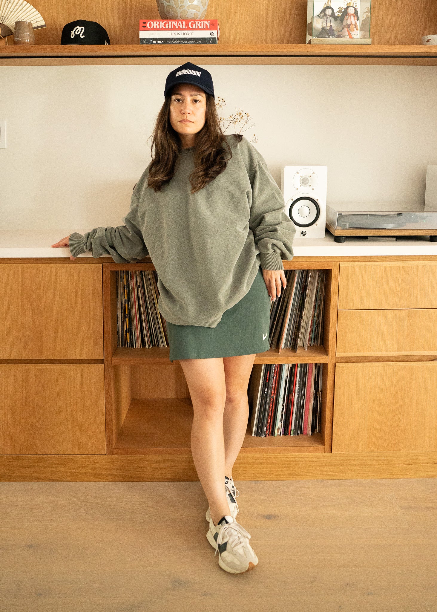 Woman in a green sweater and green skirt standing in front of a wooden shelf with records and speakers.