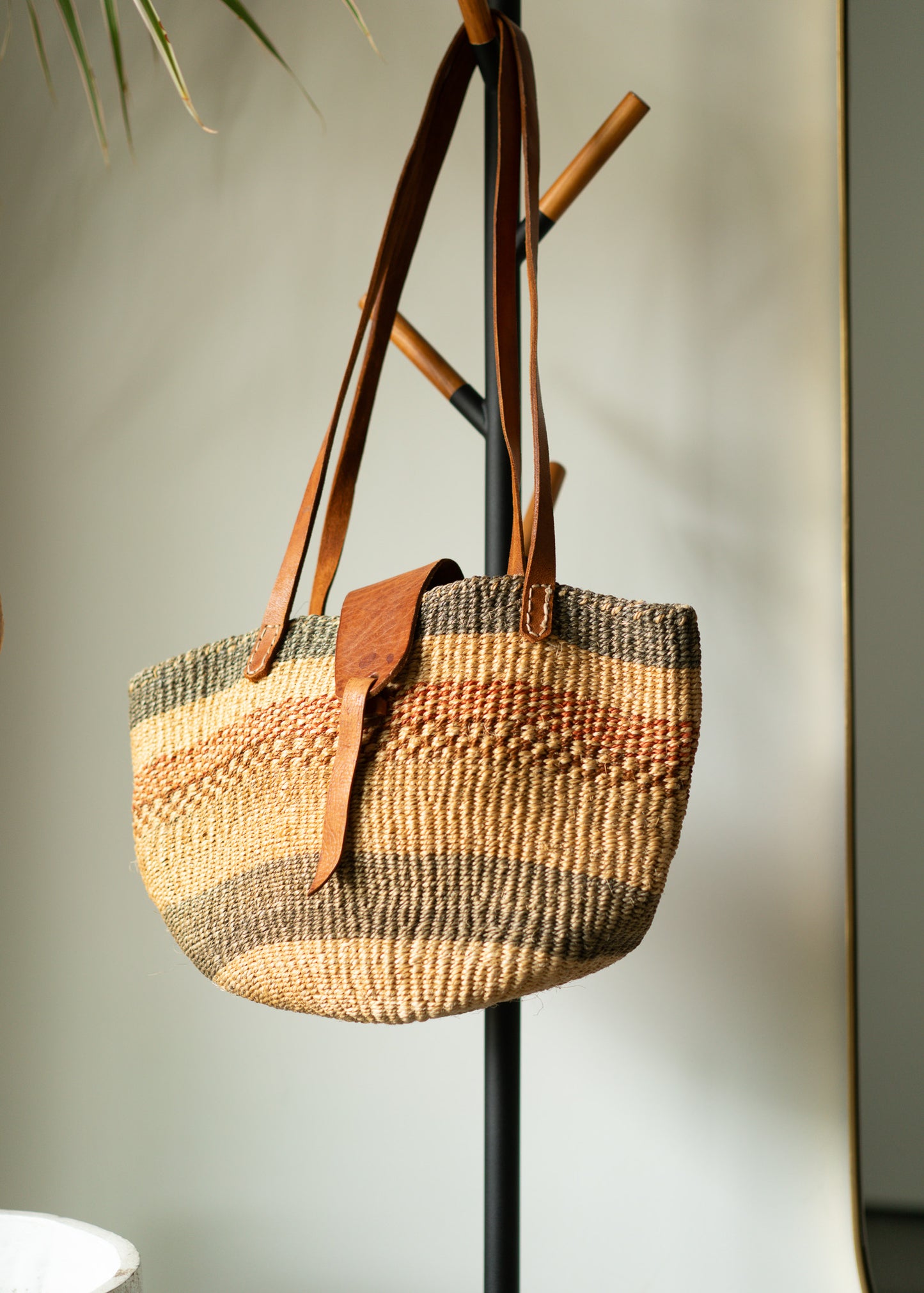 Vintage woven handbag with leather straps hanging on a stand against a neutral background