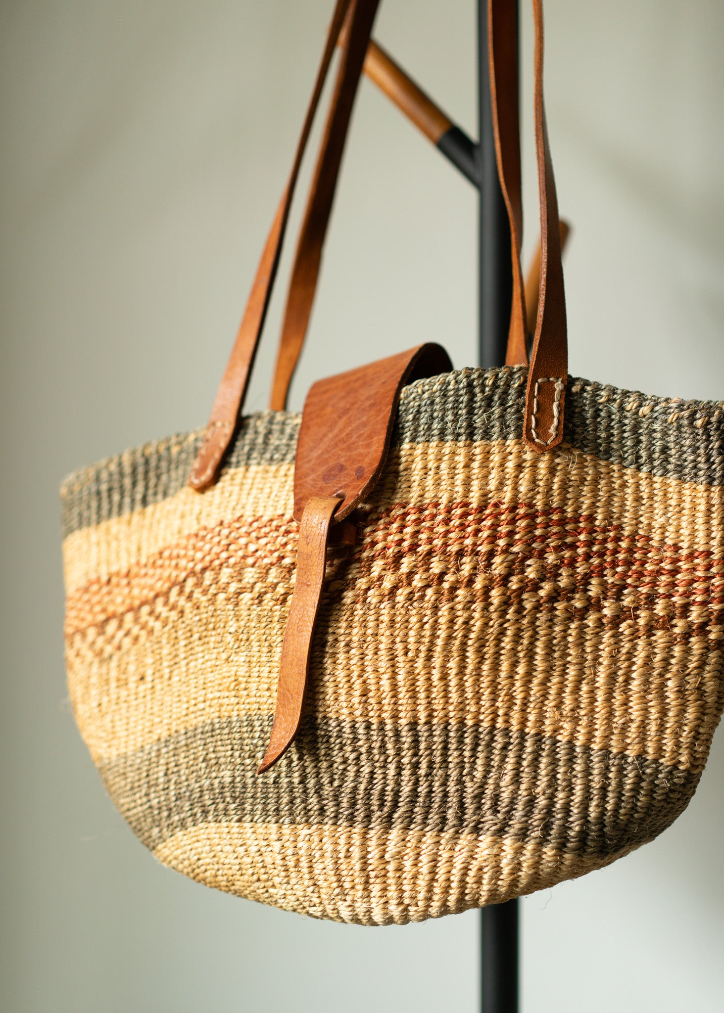 vintage oven basket bag with leather straps on a stand against a neutral background
