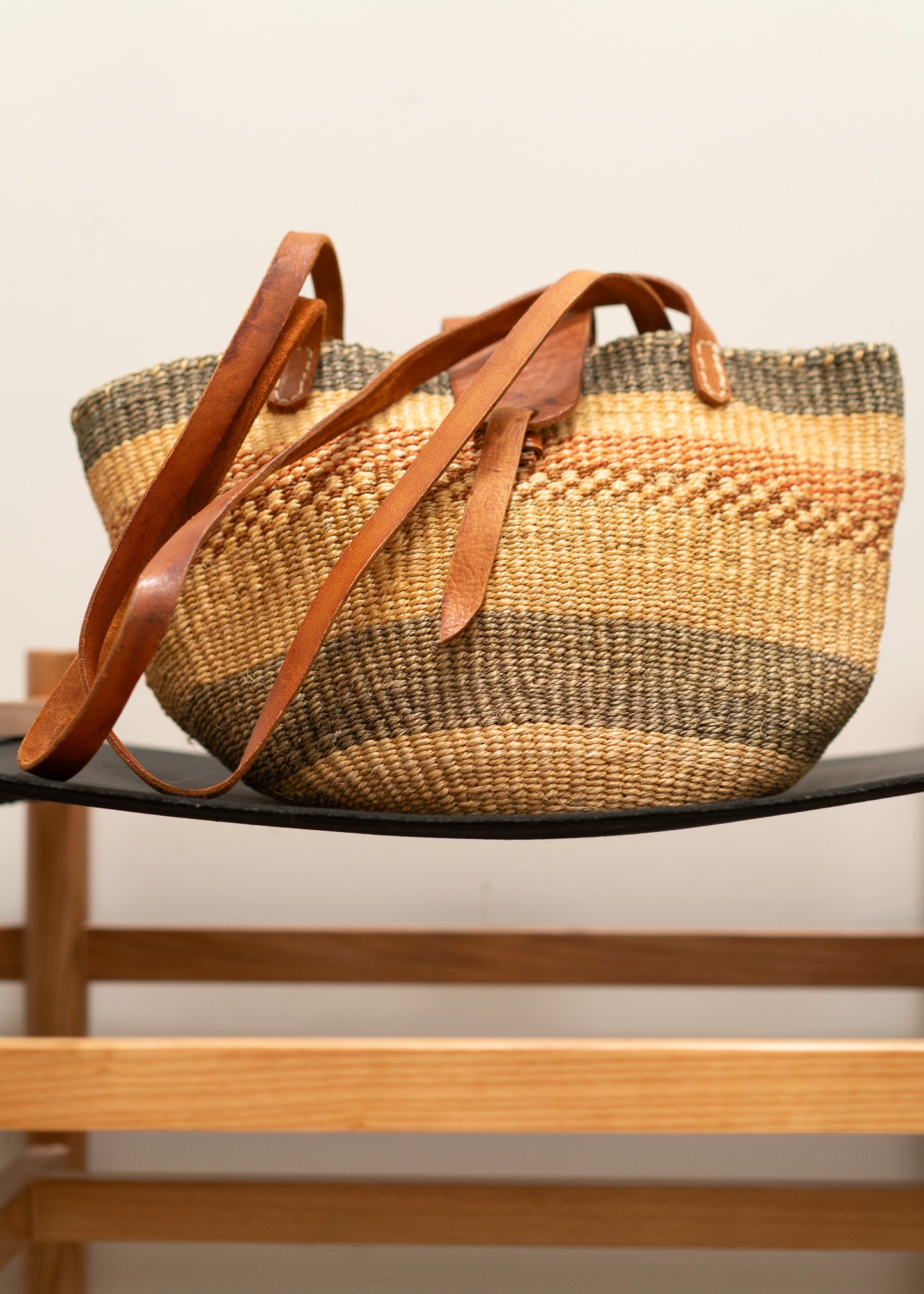vintage woven straw bag with leather straps on a wooden shelf