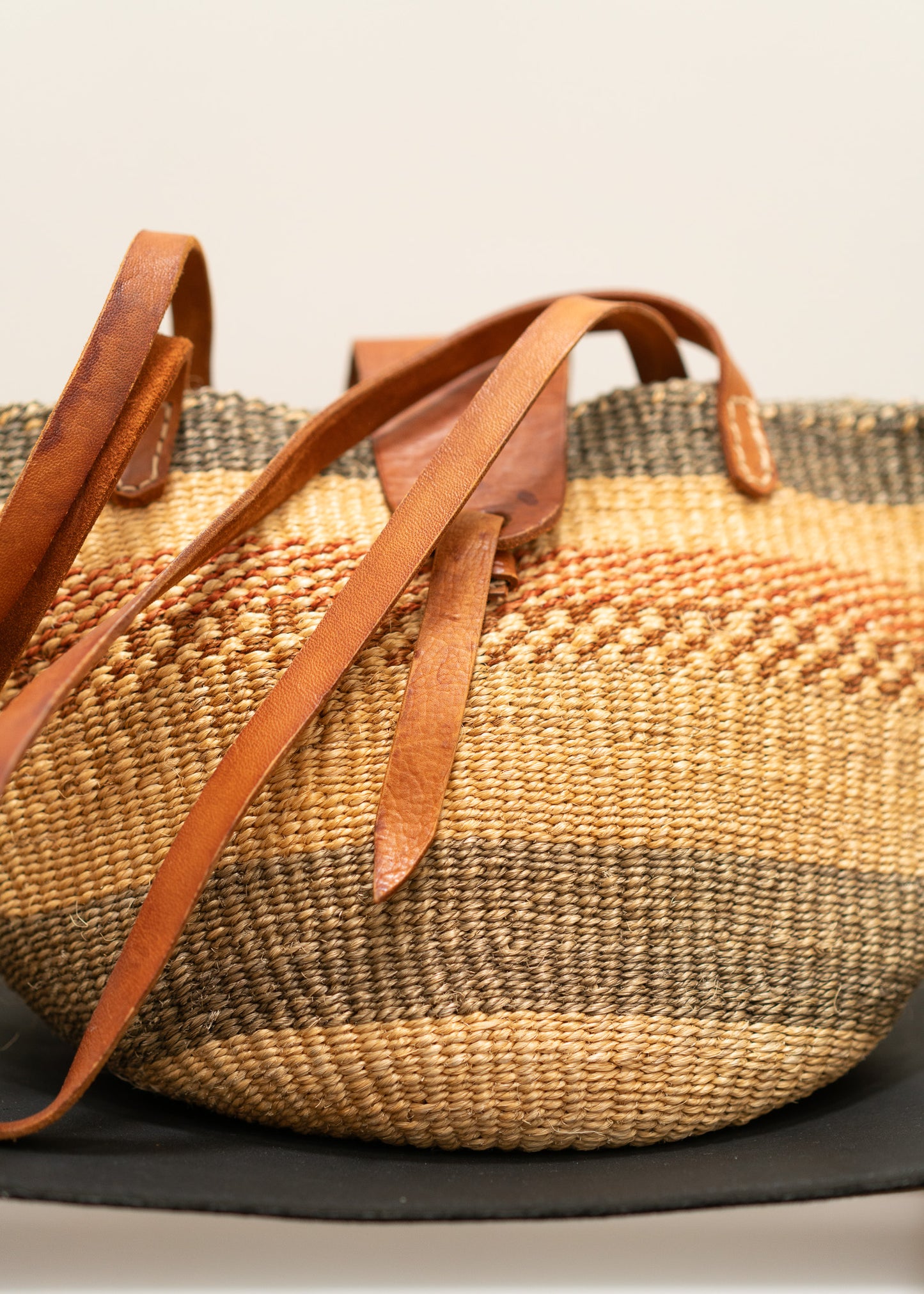 vintage woven basket with leather straps on a neutral background