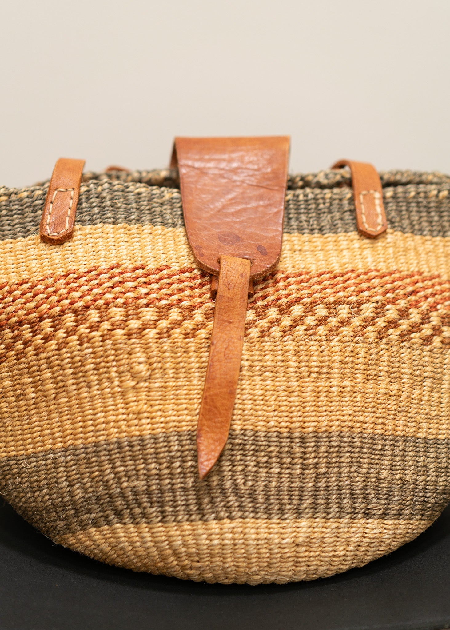 Woven basket with leather straps on a neutral background
