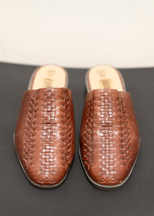 Pair of brown woven slippers on a dark surface with a light background
