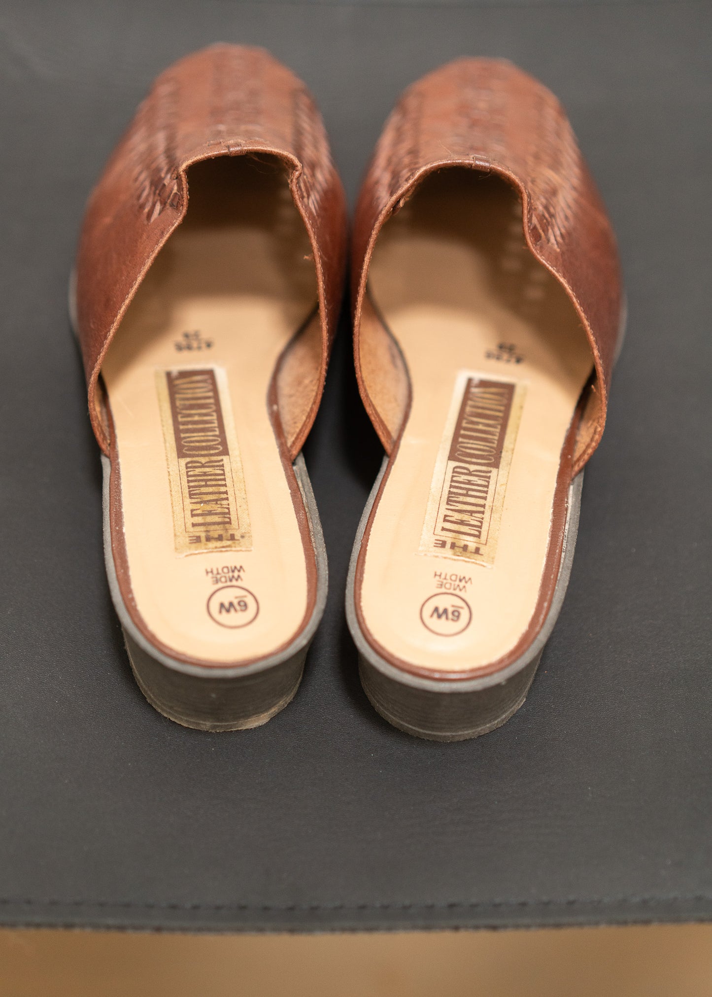 Pair of brown mules with visible brand labels on a gray surface